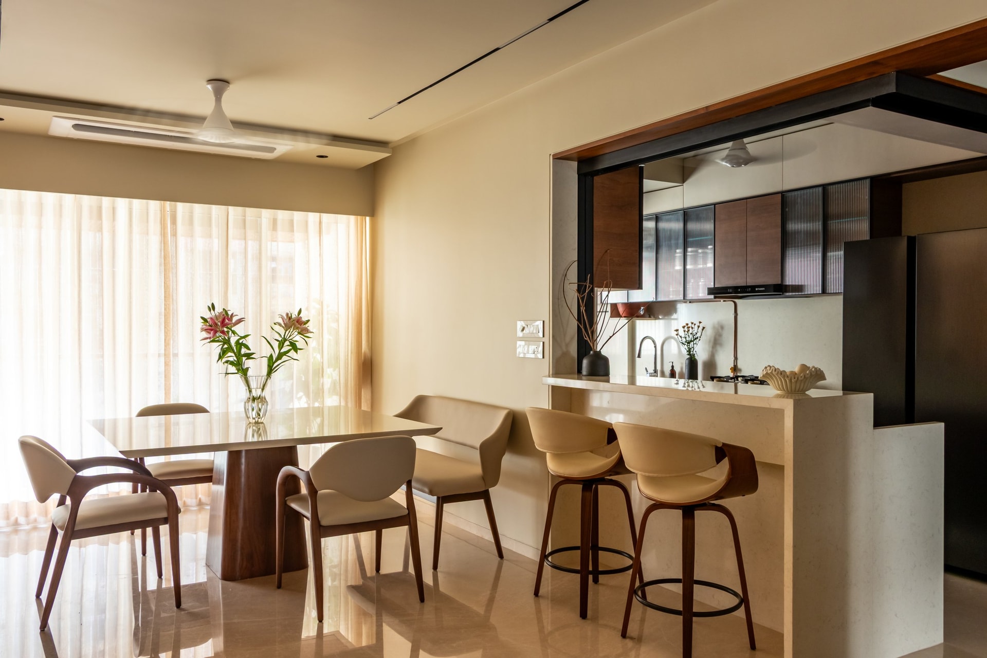 The dining area, its sculpted table and curved-back chairs set beside a stone-clad breakfast counter that extends from the open kitchen