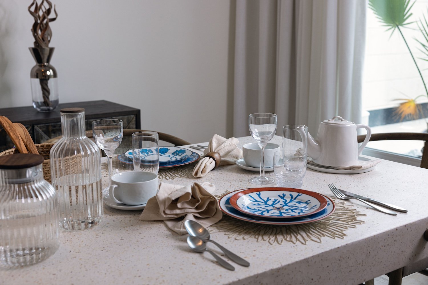 The dining table set with terrazzo, ribbed glassware, linen napkins, and ceramic plates painted with cobalt coral motifs