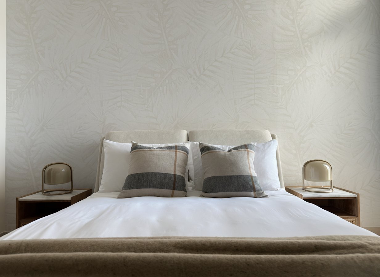 The guest bedroom, where a cream bouclé wingback bed sits against wallpaper printed with a pale palm-frond motif