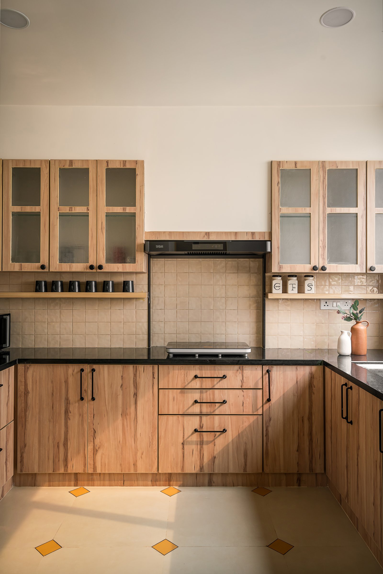 The kitchen in light wood-grain laminates with black granite counters and a beige square-tiled backsplash