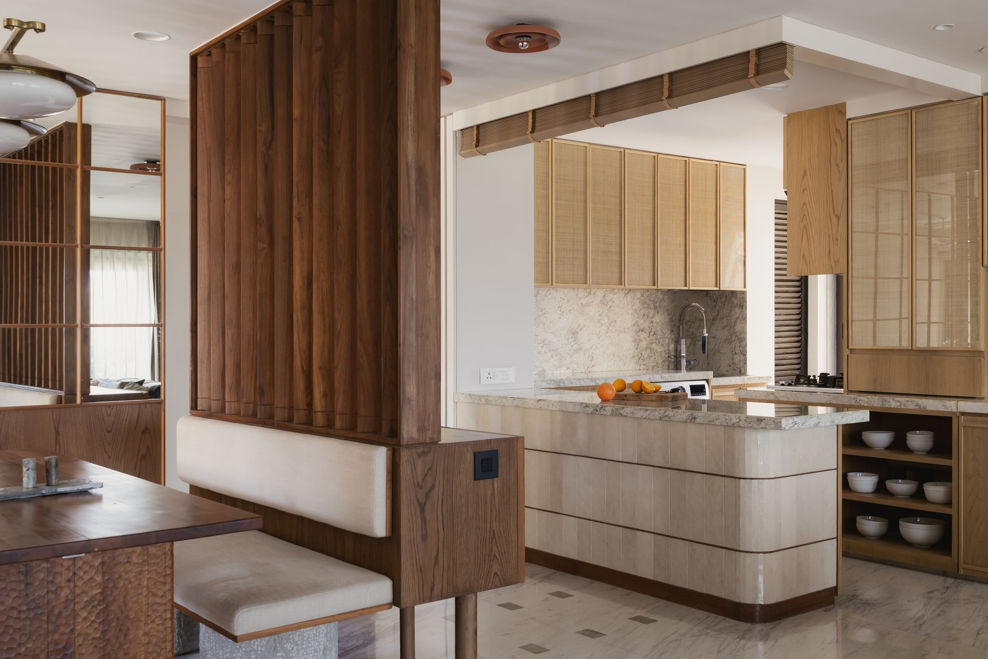 The kitchen, its fluted island and rattan-fronted upper cabinets continuing the material language of the entry