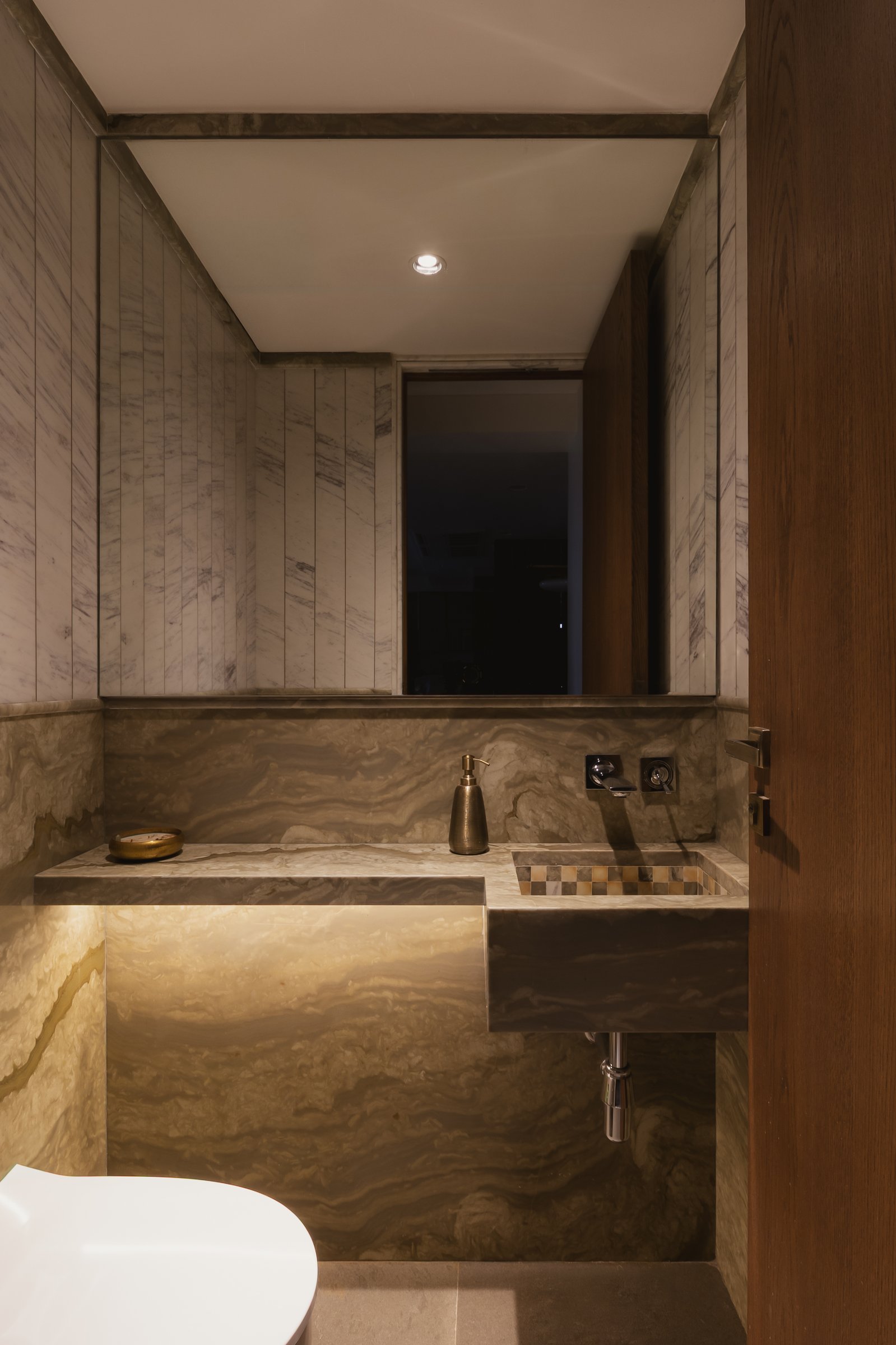 The powder room, wrapped in richly veined stone, with a bespoke basin inset with a mosaic of waste marble offcuts