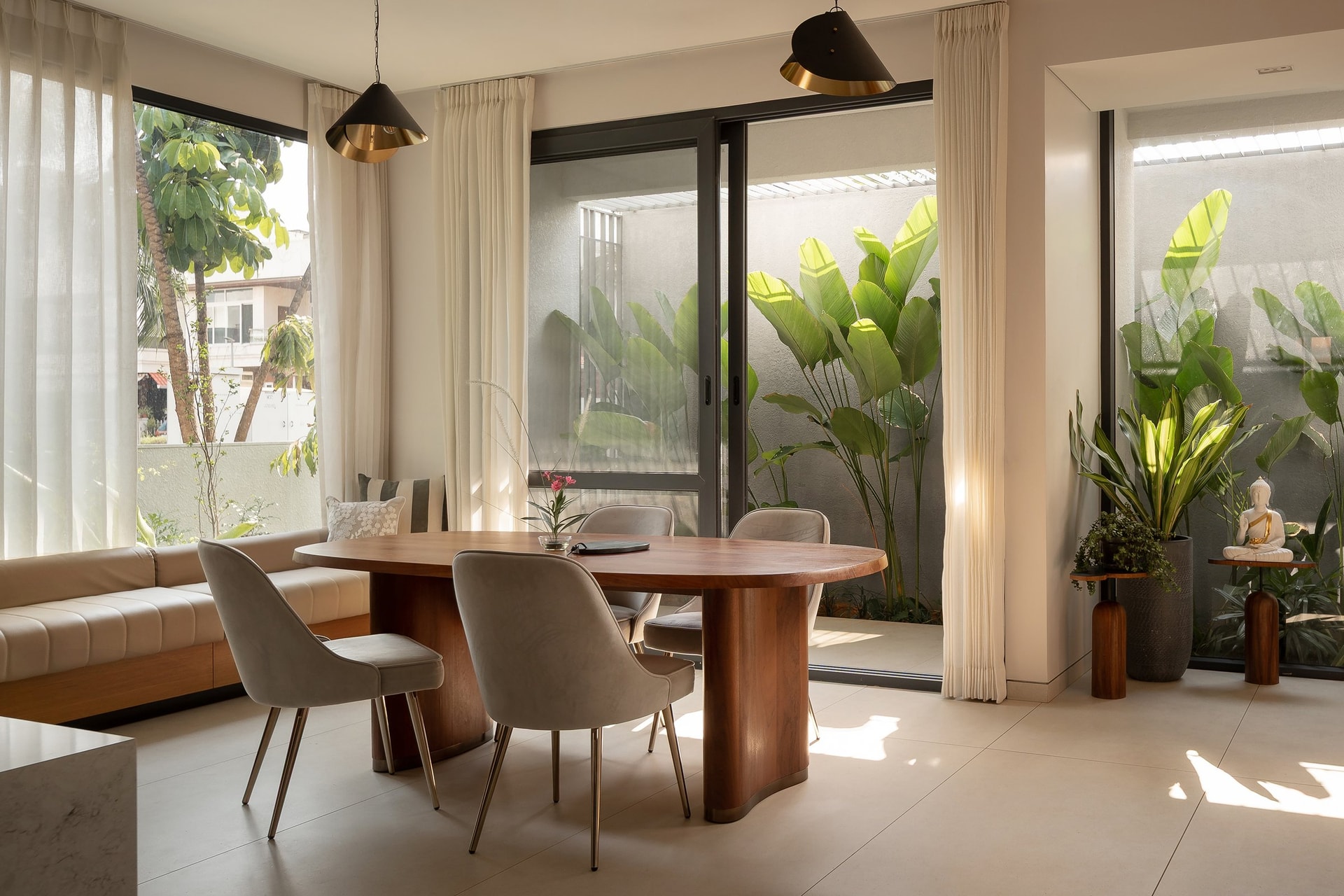 The dining area, with a rounded solid-wood table and velvet chairs set beside a long banquette along the window wall