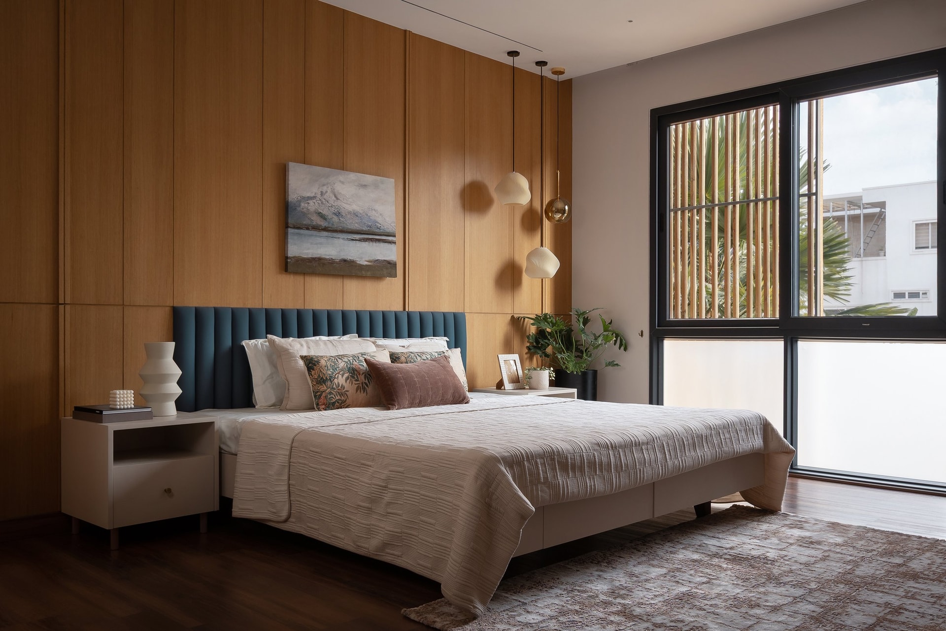 The primary bedroom, its channel-stitched teal headboard set against a full-height timber panelled wall