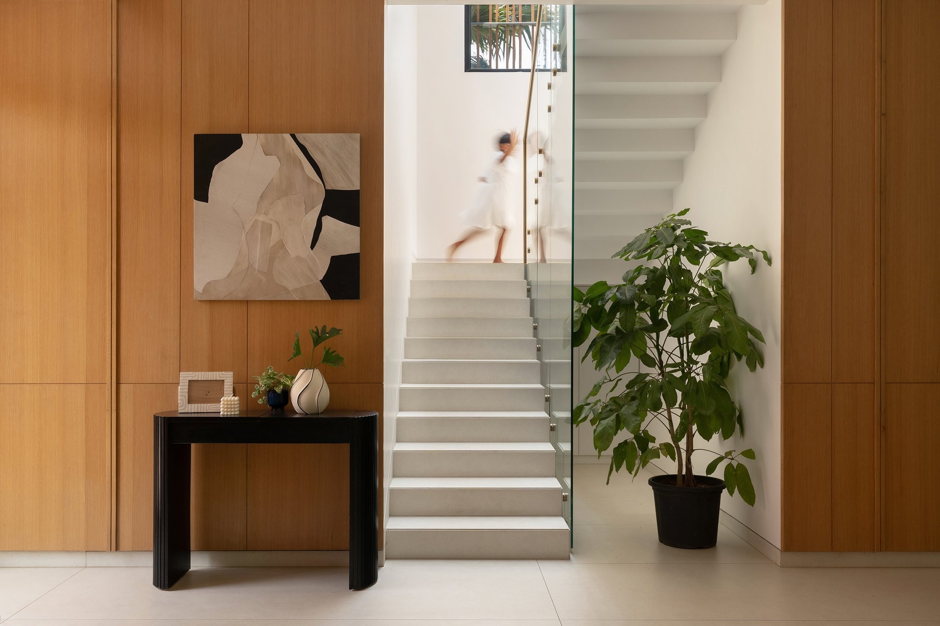 The staircase, lifted behind a frameless glass balustrade and lit by daylight from above