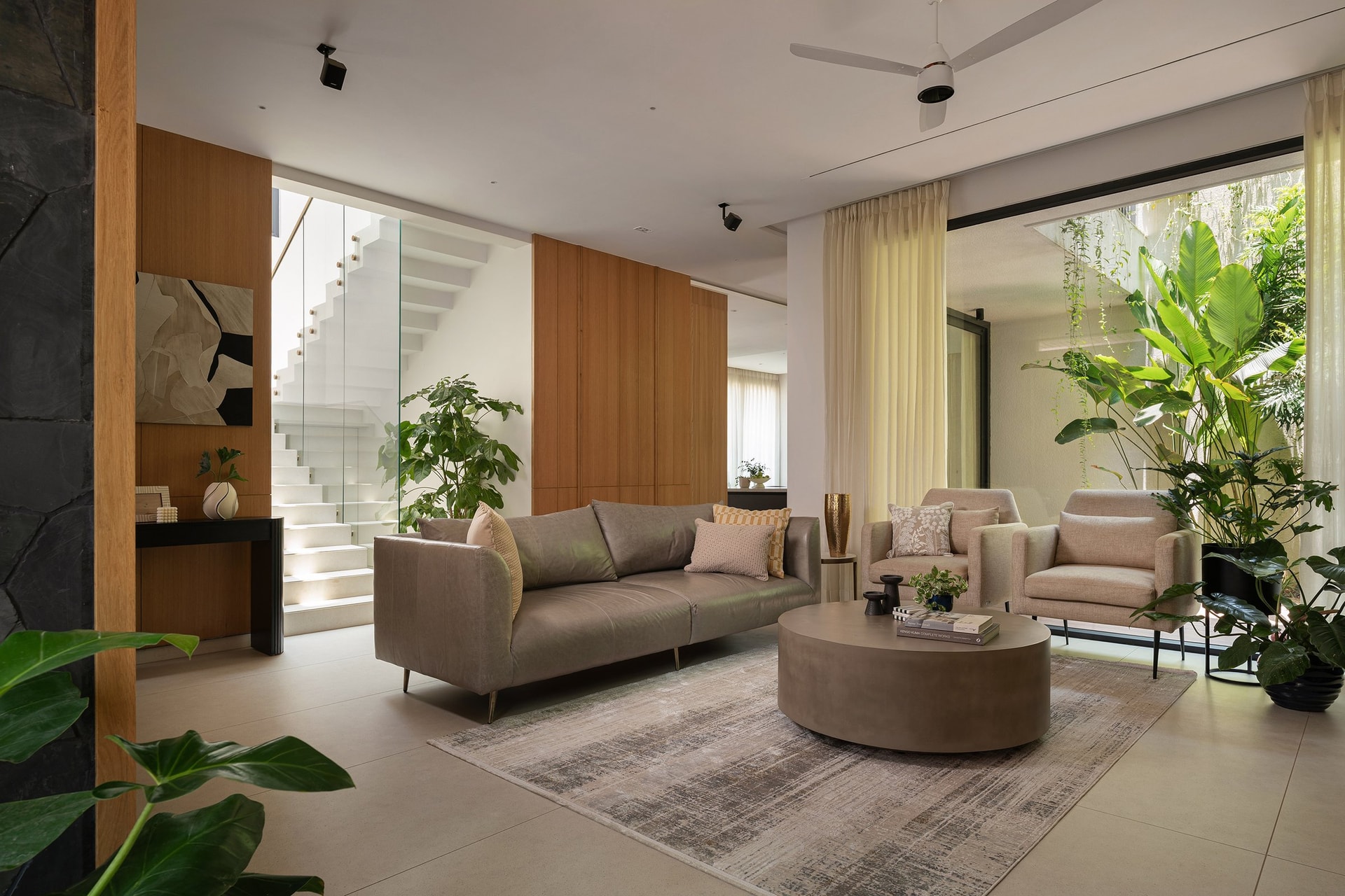 The living room, where a soft taupe leather sofa sits against timber joinery and a black stone wall, the staircase visible beyond