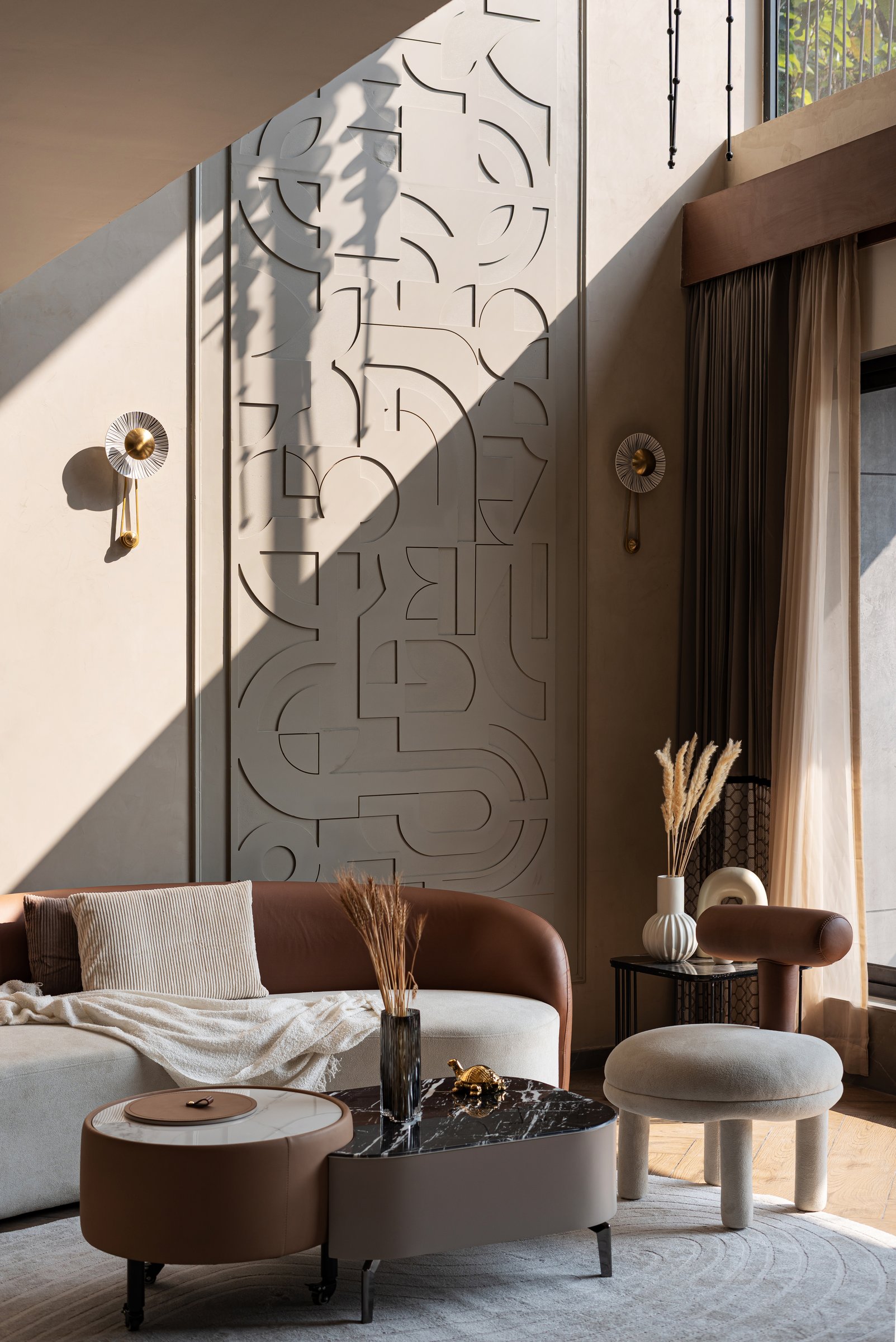 The formal living room, where a double-height relief panel and brass sconces give the volume its measured verticality