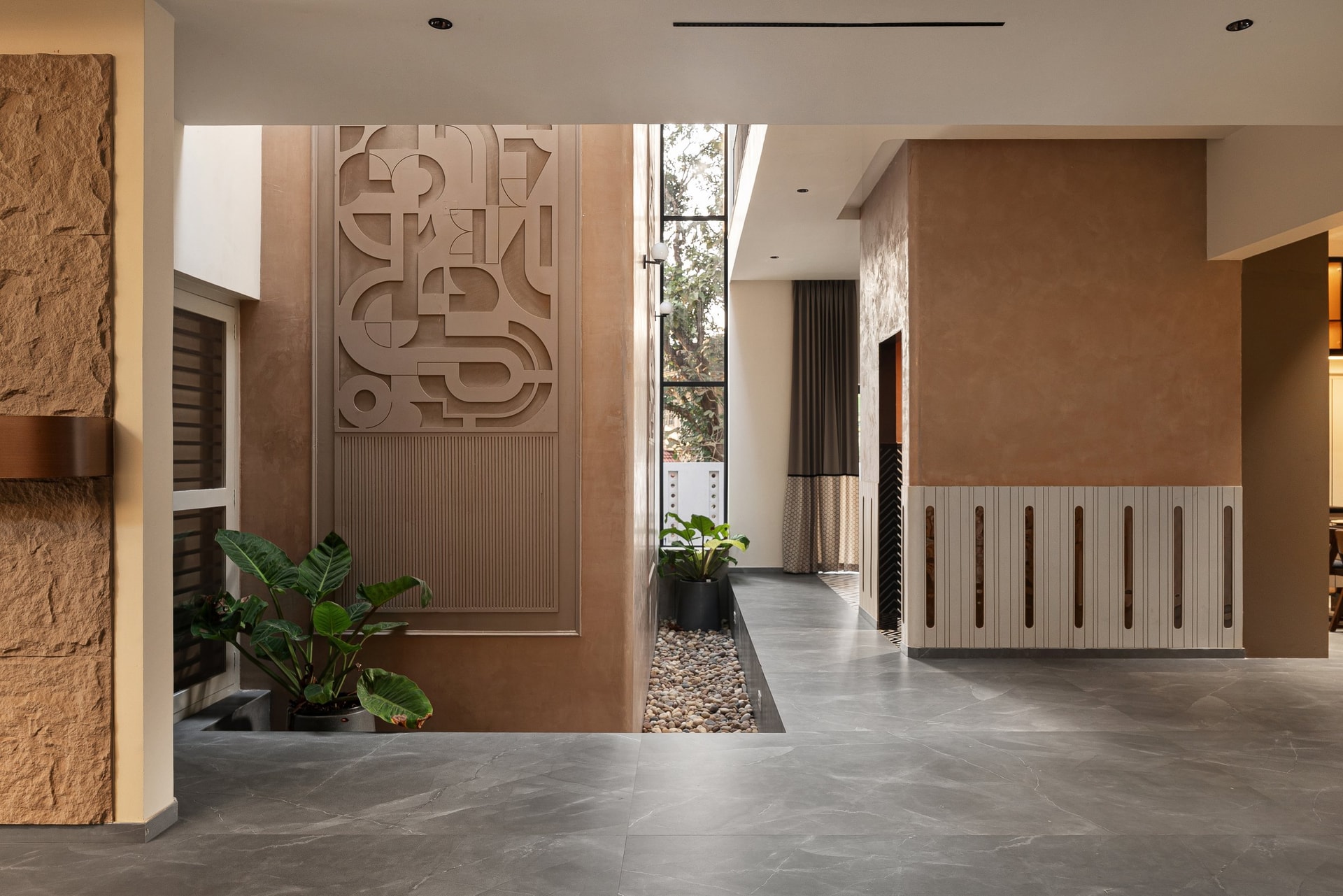 The entry foyer, where a sculpted relief panel rises beside a vertical slot of glazing that draws light into the heart of the plan