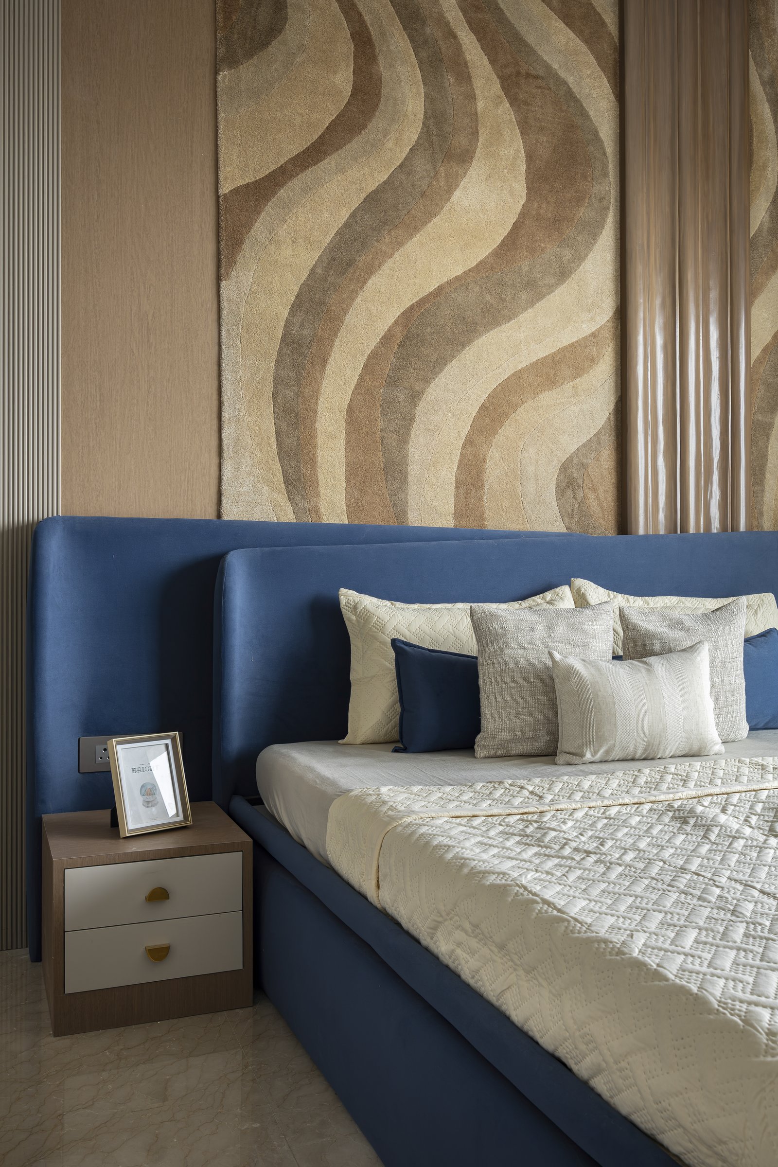 The master bedroom, where a customised wall-rug backdrop in flowing bands of ochre and umber meets a deep blue upholstered headboard
