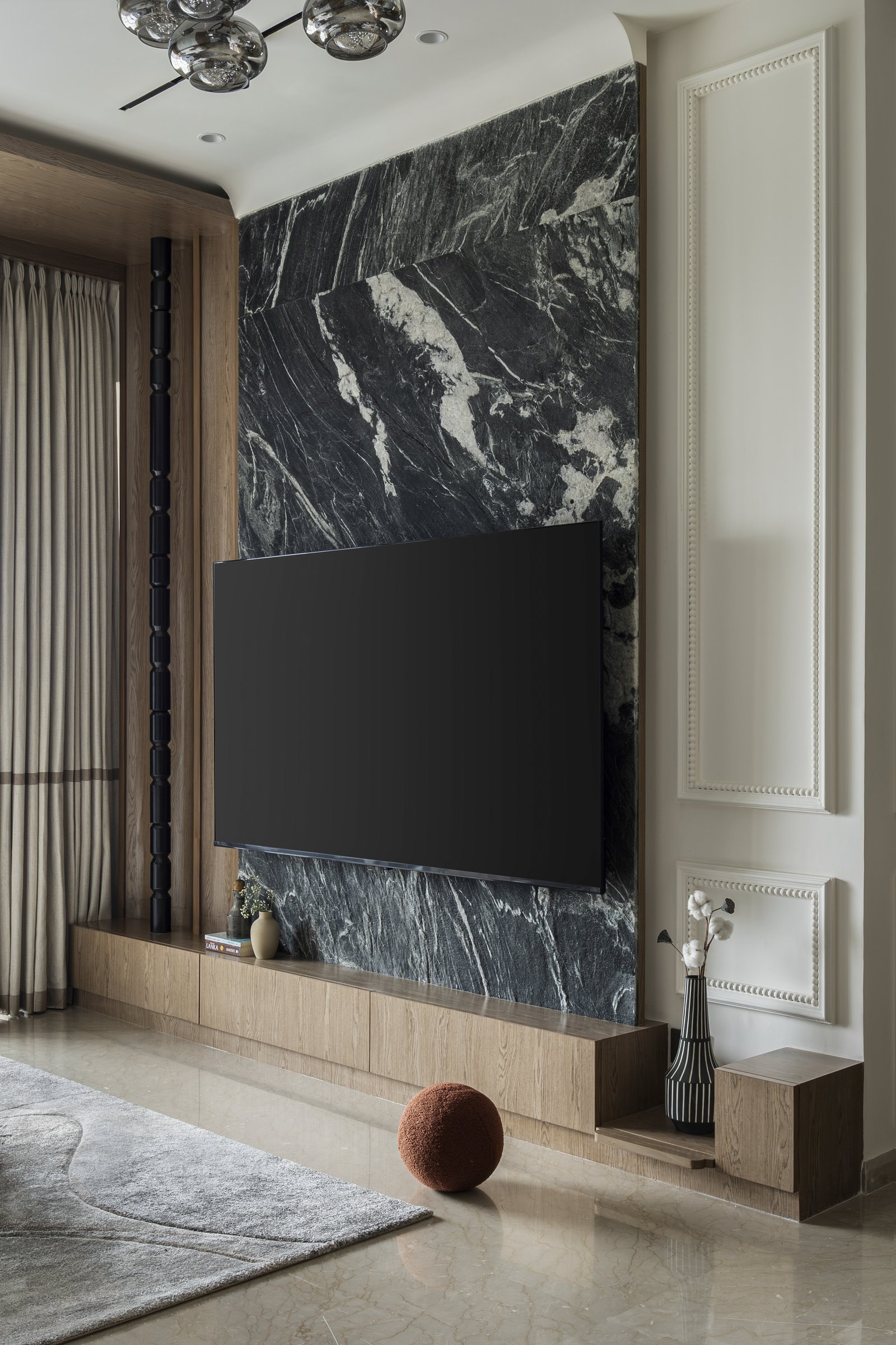 The media wall, where dramatically veined dark stone is flanked by beaded moulded panels and a slim fluted column