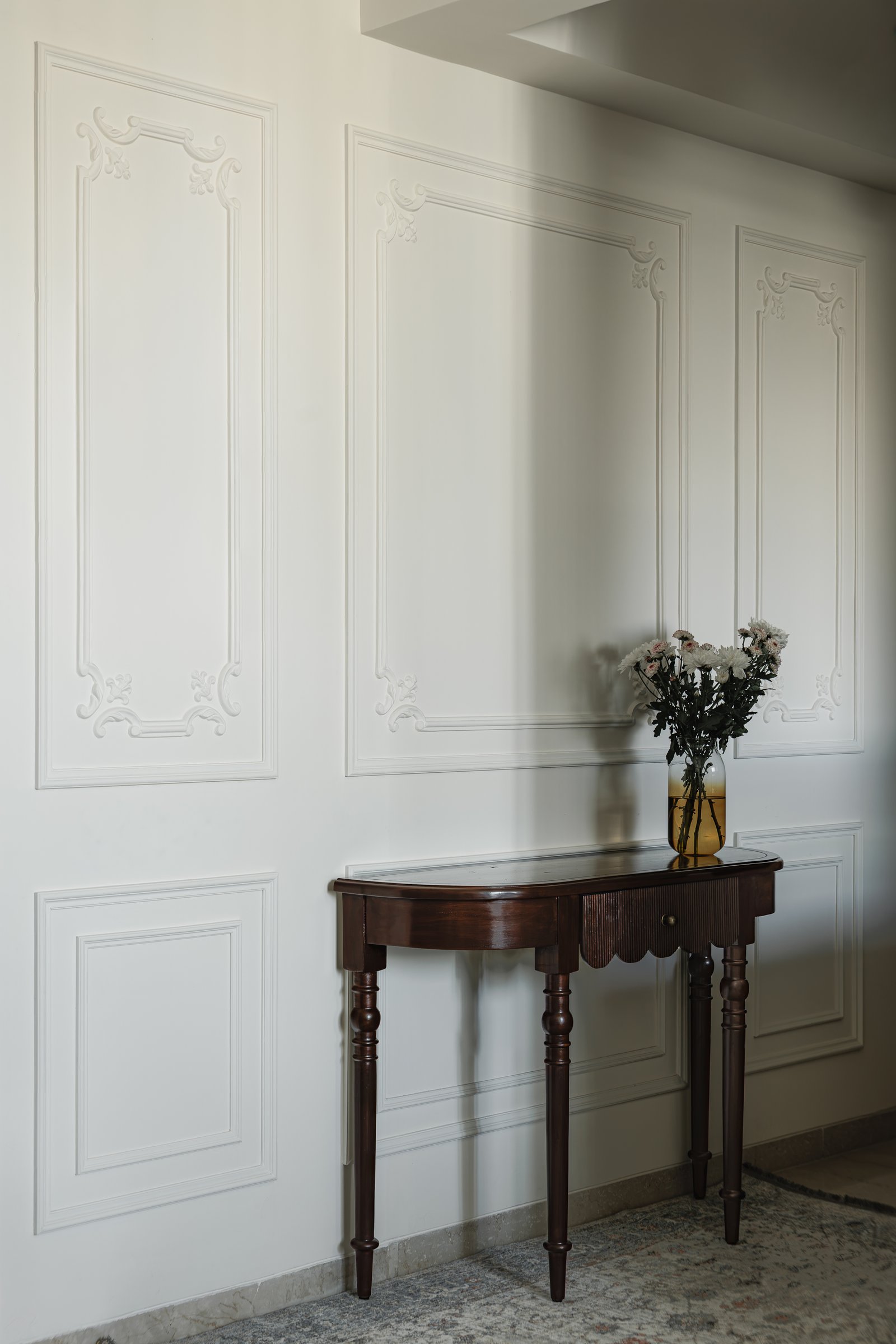 The entry wall, where applied ornamental panelling meets a turned-leg demi-lune console in dark wood