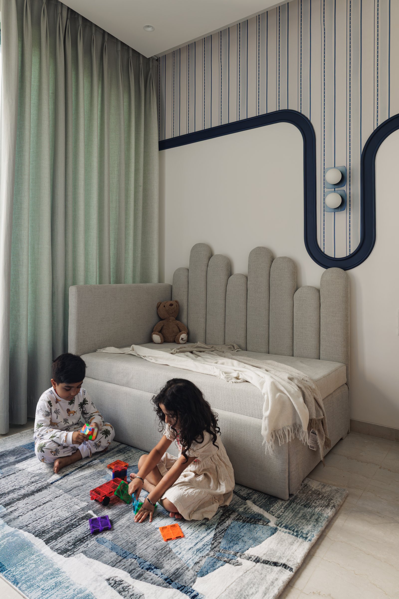 The children's bedroom, with a scalloped upholstered headboard and a navy curved moulding tracing the pinstripe wallpaper