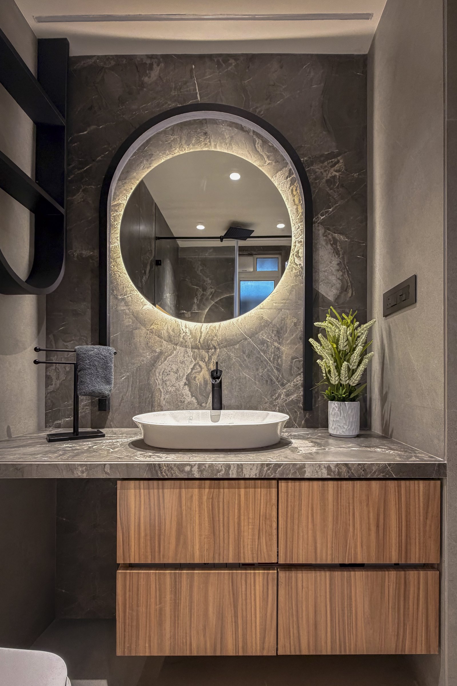 The guest bathroom in grey veined stone, with an arched backlit mirror above a veneered vanity