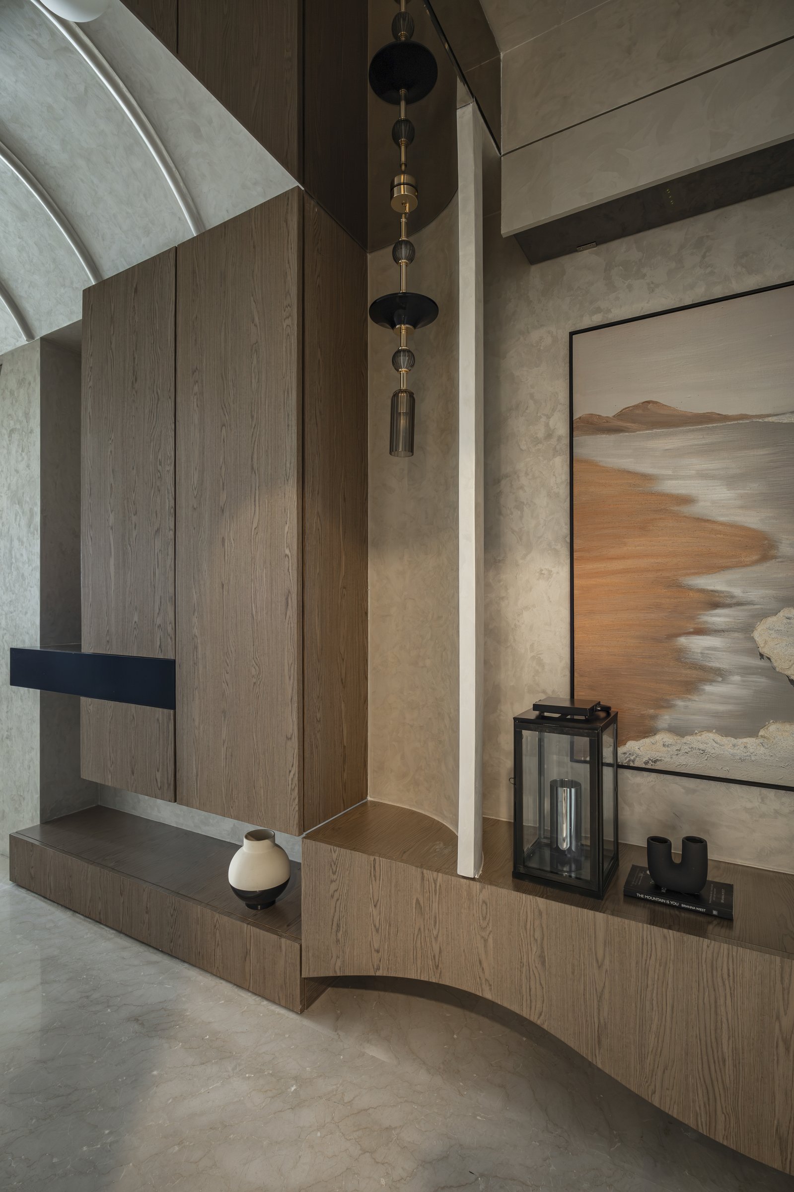 A vaulted passage holding a veneered console with a tiered pendant of blackened discs and brass