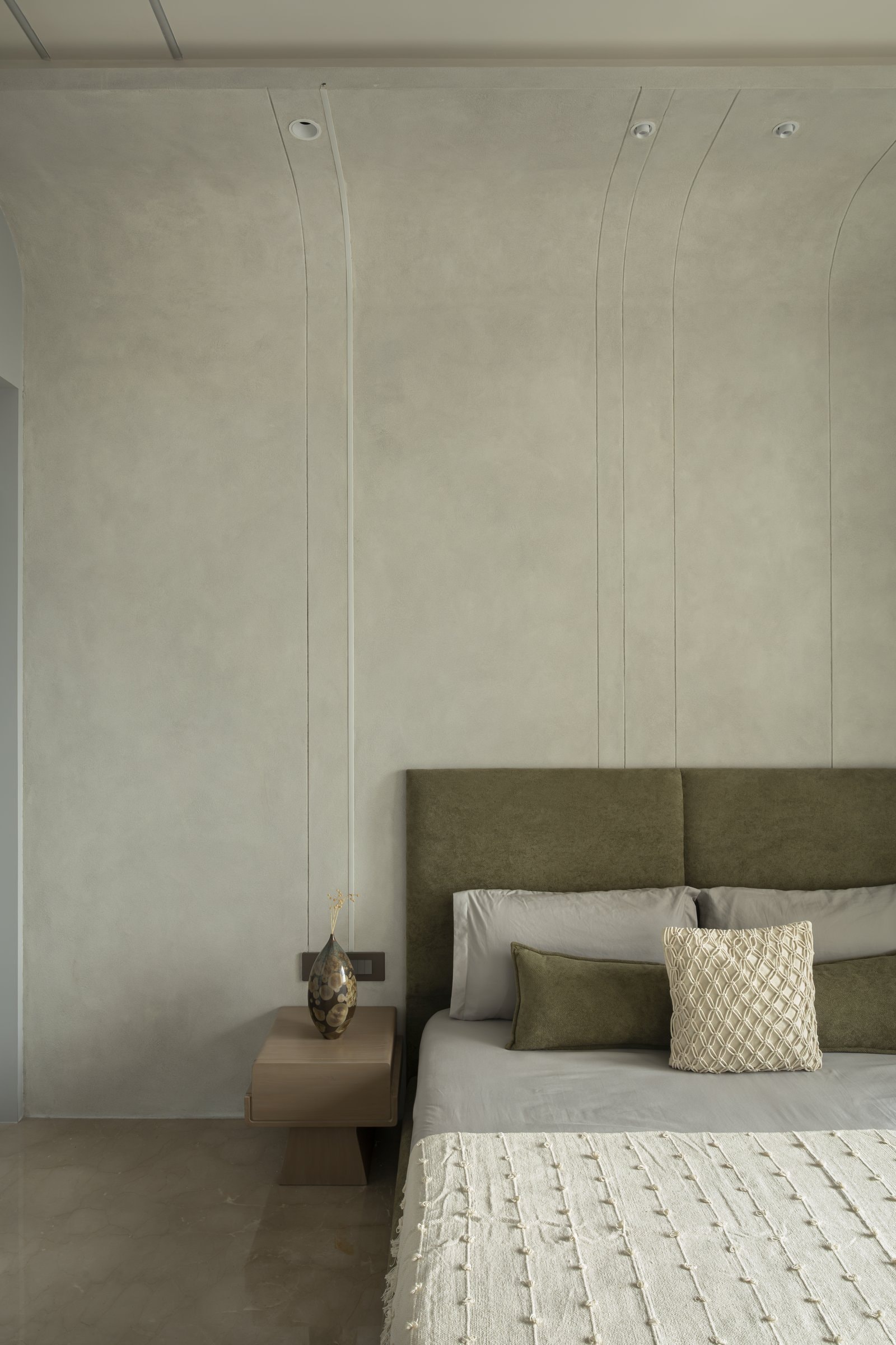 The third bedroom's textured plaster wall, with vertical reveals rising into the ceiling behind a deep olive headboard
