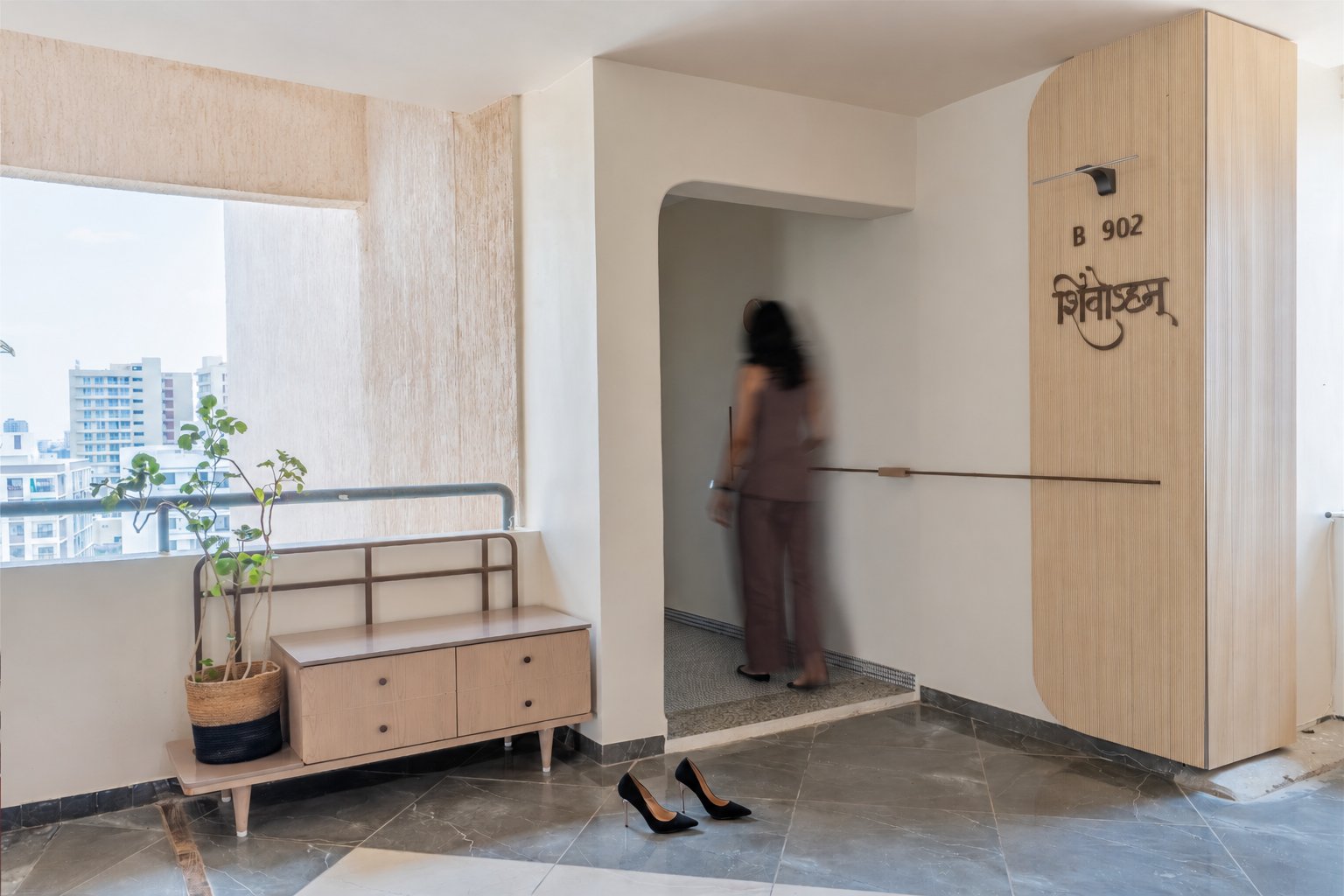 The arrival threshold, where a reeded panel carries the home's name in Devanagari and a mosaic inset marks the shift from corridor to private realm