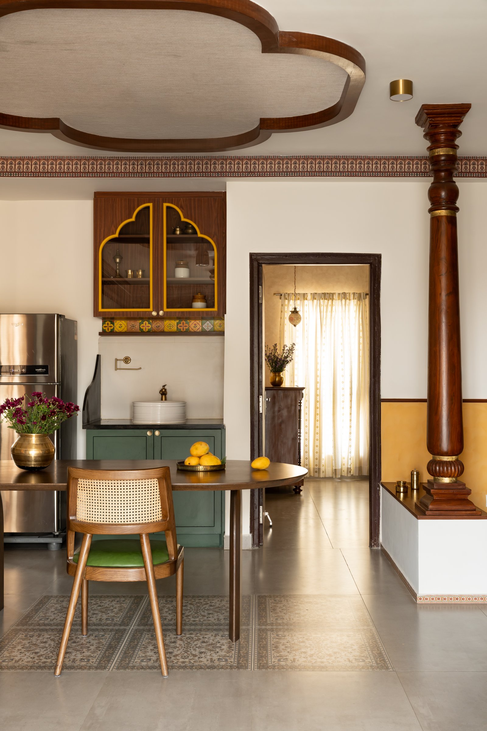 The dining area, where an oval wooden table on sculpted arched bases sits beneath the scalloped ceiling detail
