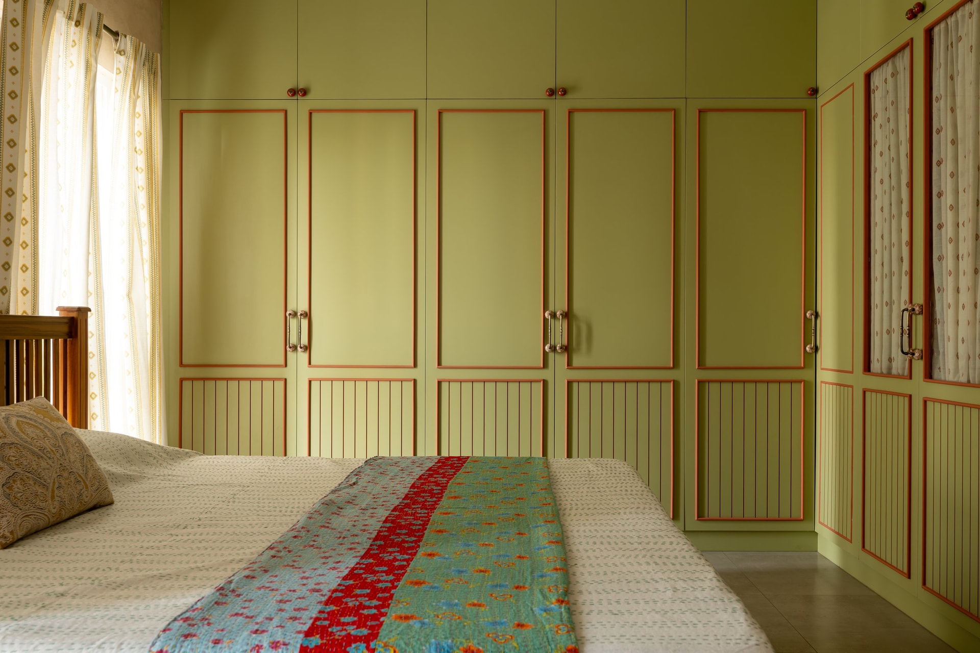 The sage green wardrobe wall, with terracotta trim outlining each panel and a slatted lower section introducing rhythm