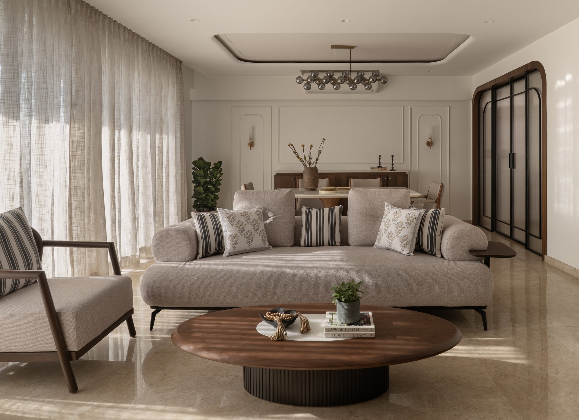 The living room, where a curved oatmeal sofa and sculpted globe chandelier establish the home's unhurried rhythm