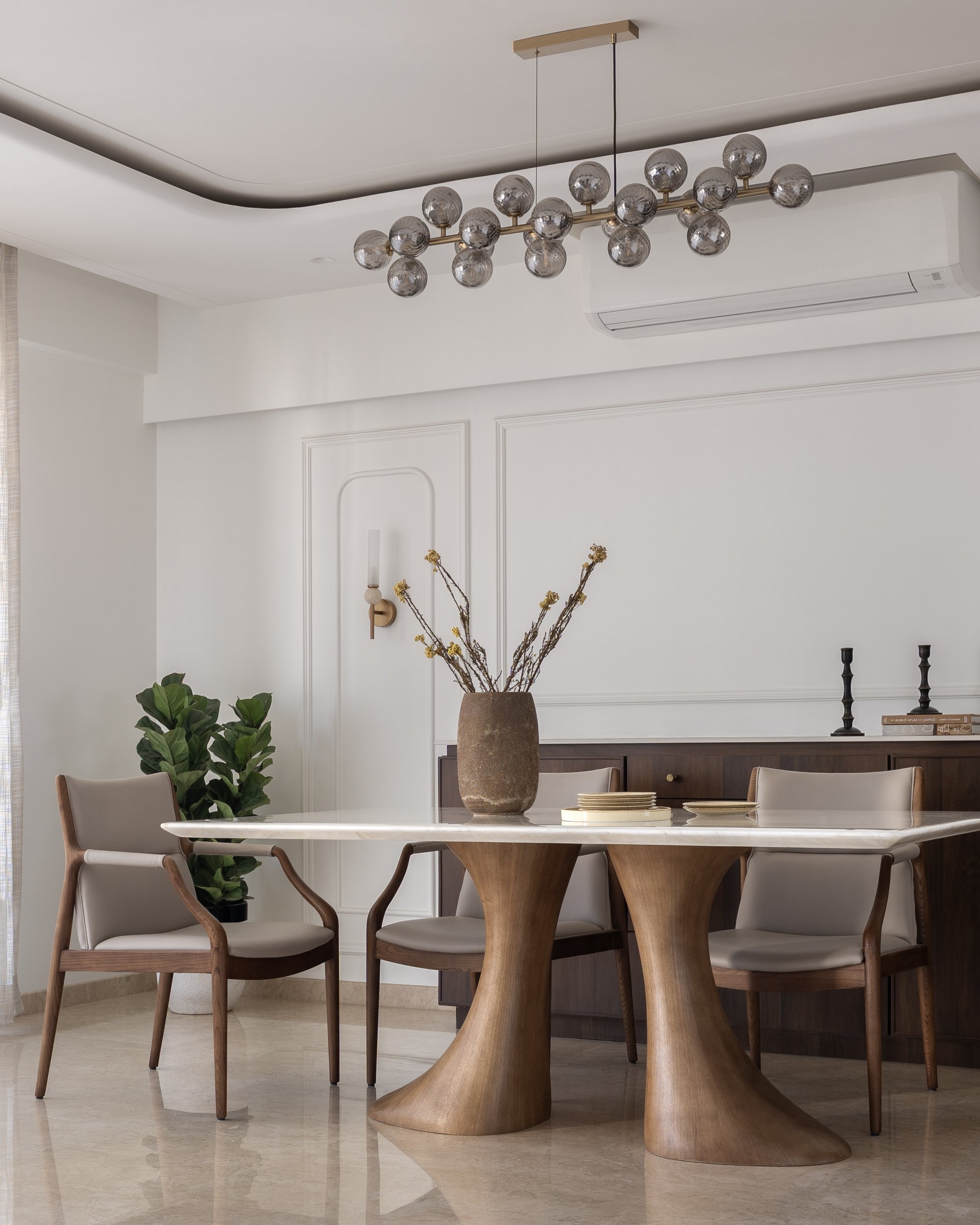 The dining area, anchored by a sculpted twin-pedestal table and a linear smoked-glass chandelier
