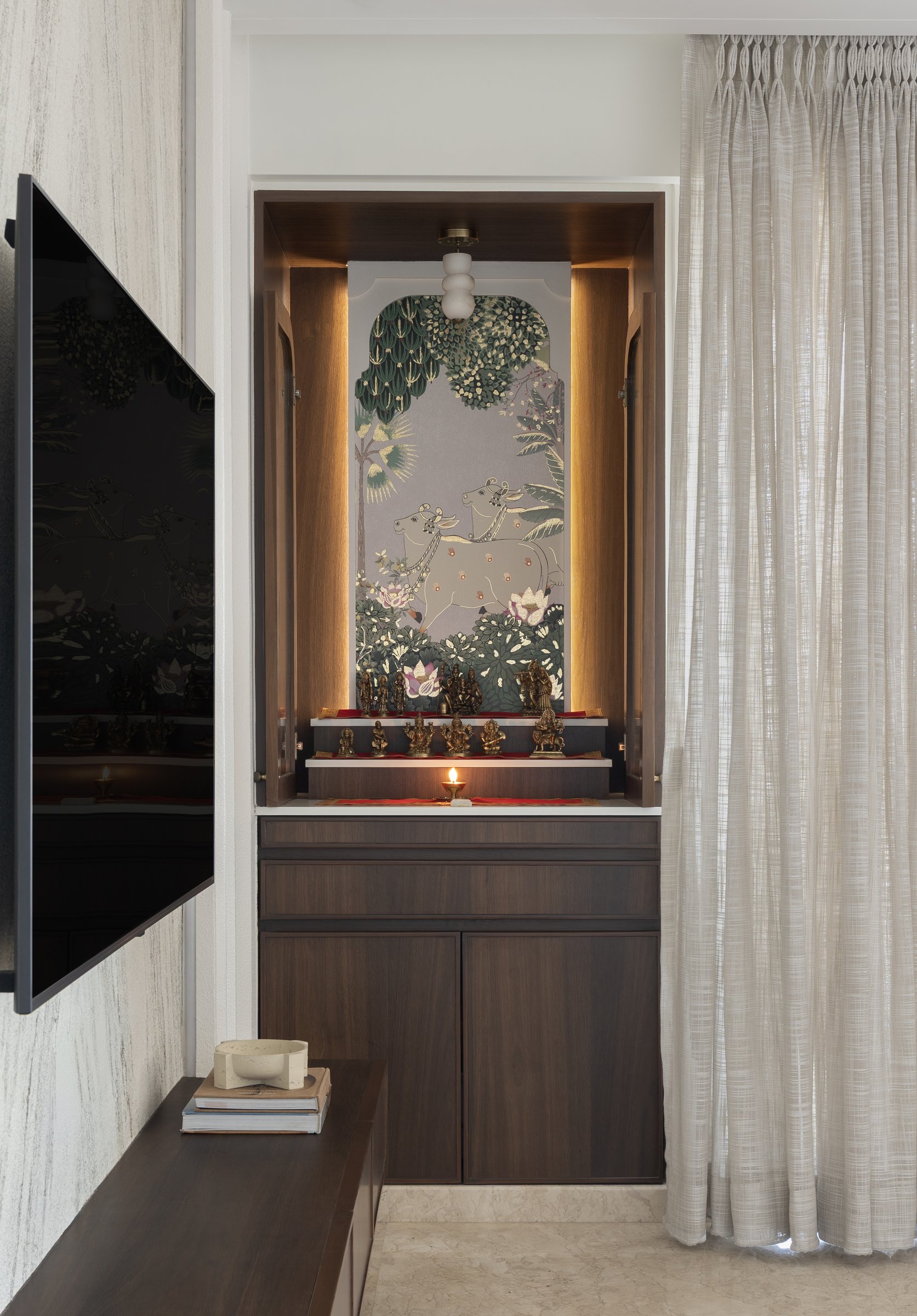 The puja alcove, where a pichwai-style artwork sits within a lit wooden niche
