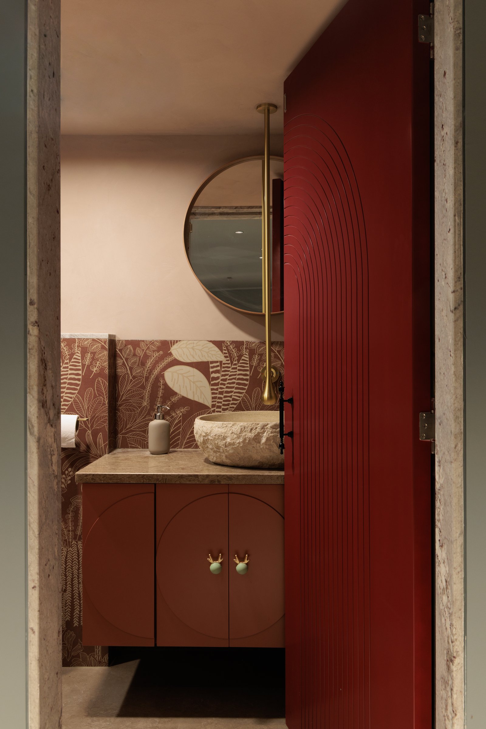 The powder room, where a terracotta vanity with brass antler knobs and a patterned wallpaper condense the studio's palette into a single expressive moment