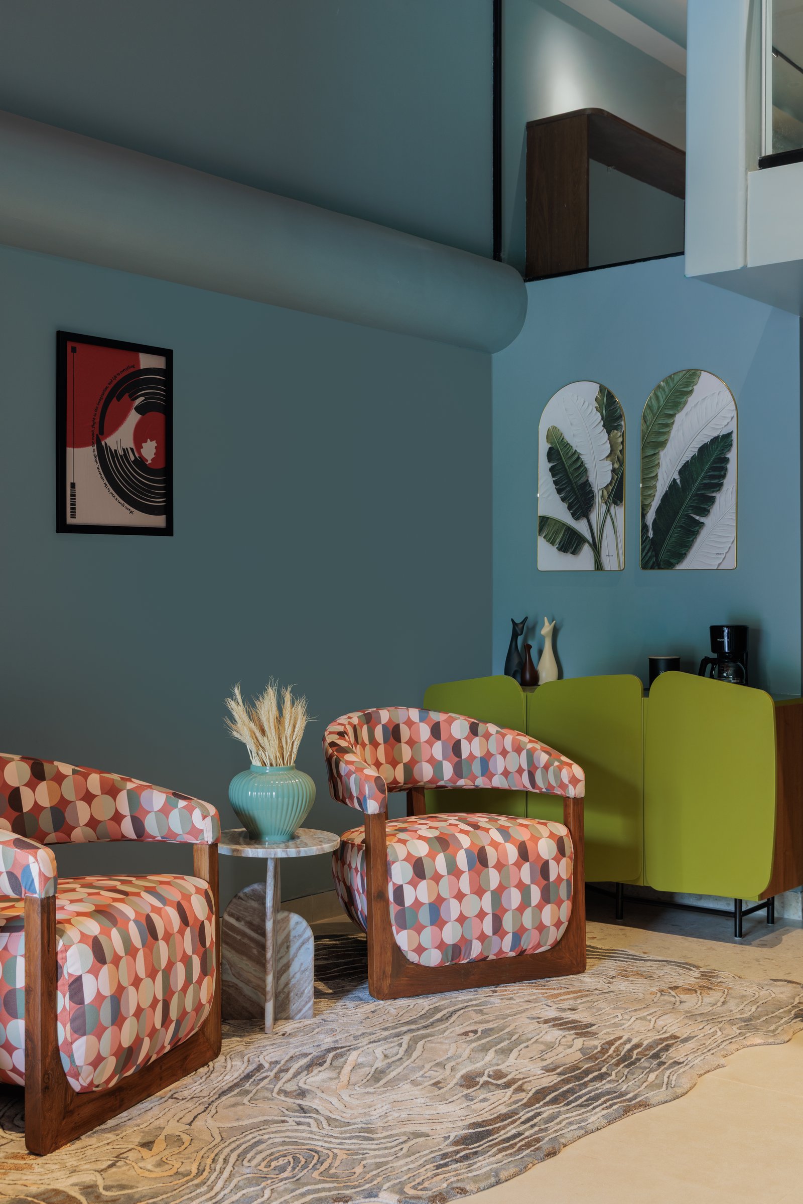 The lounge, where geometric-patterned armchairs and a lime-green sideboard introduce the studio's confident use of colour against muted blue-grey walls