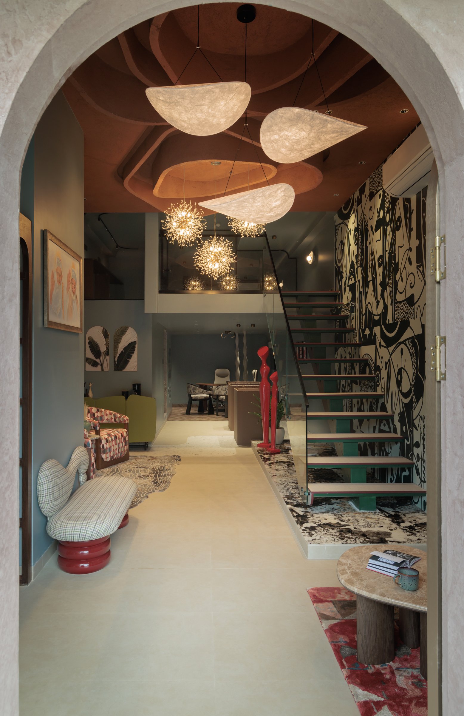 The studio seen from the entrance arch, where sculpted ceiling recesses, suspended paper-form pendants and a graphic mural establish the double-height volume