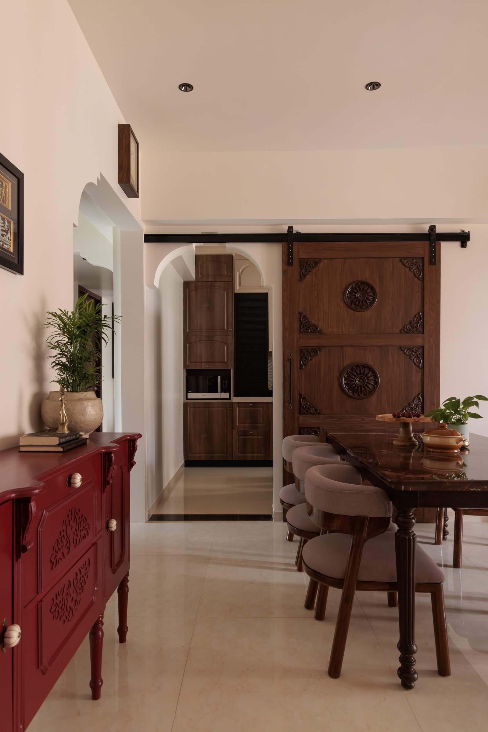 A hand-carved sliding door on a steel track marks the threshold between dining and kitchen, introducing an unmistakably Indian voice