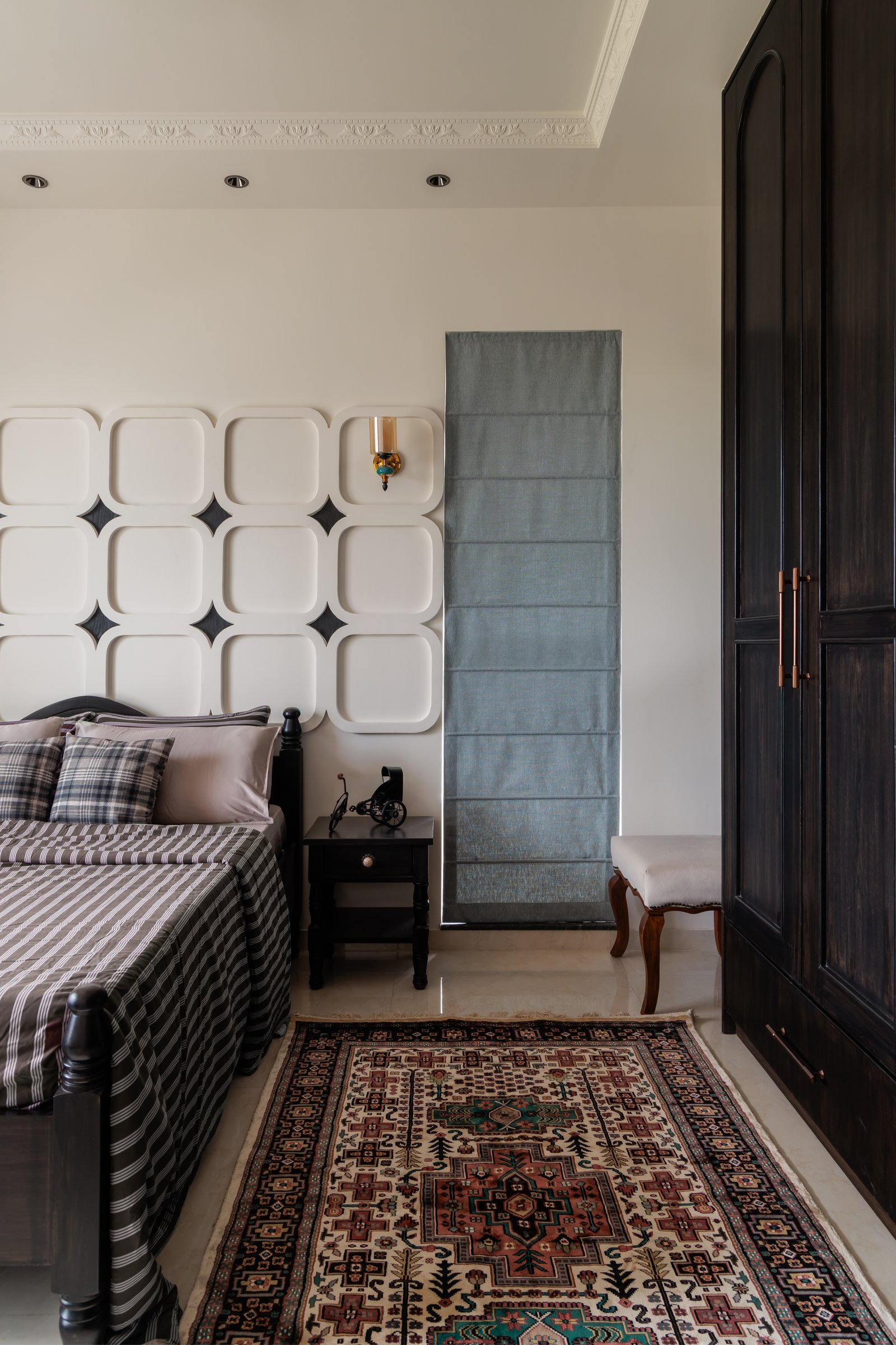 A side view of the guest room, pairing the sculpted panelling with a dark wardrobe and a muted blue roman shade