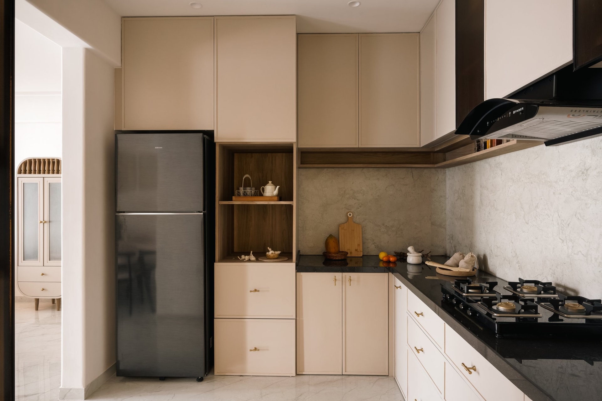 The semi-open kitchen, where cream shutters and brass pulls meet a wood-toned open niche and a dark stone counter