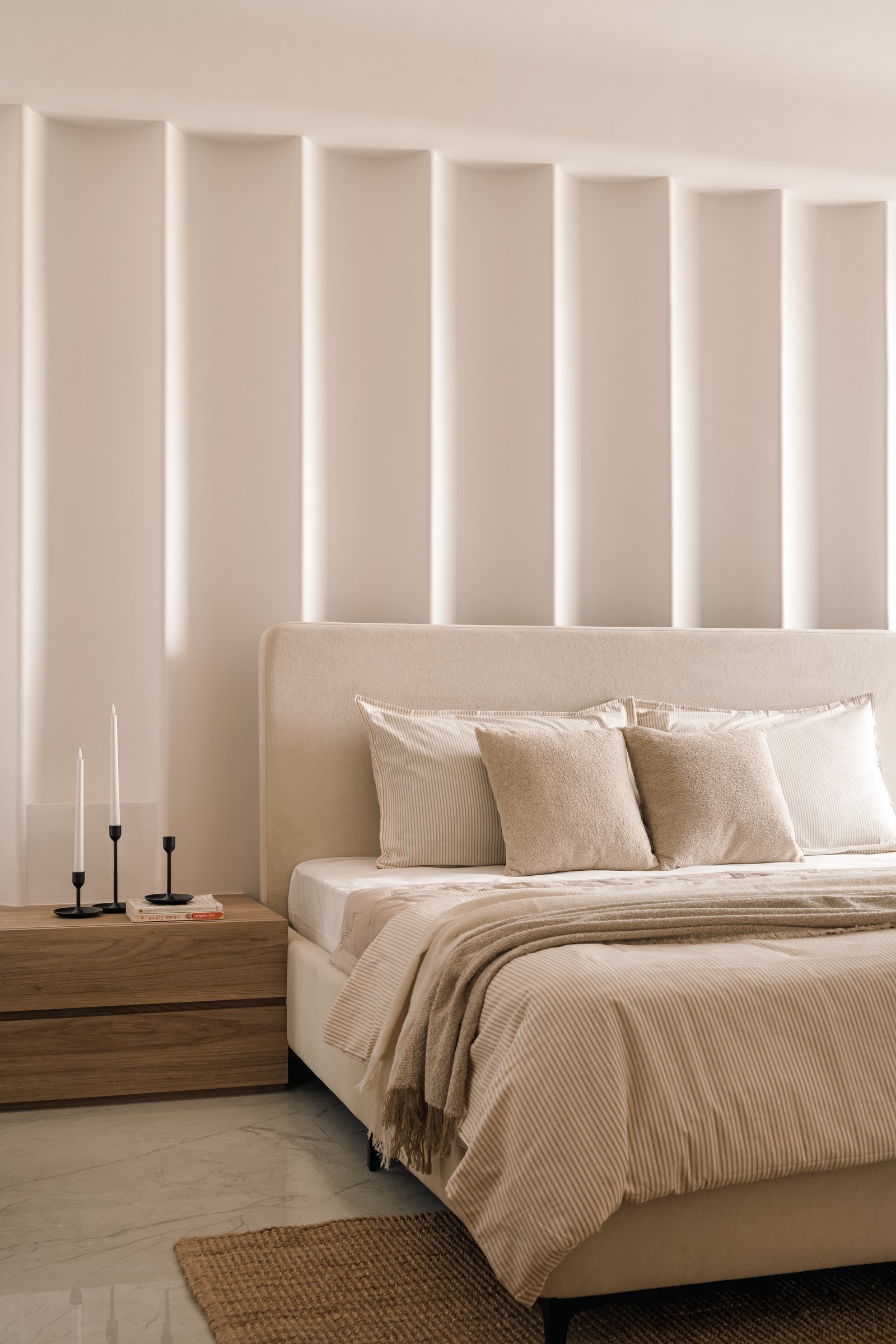 The primary bedroom, where a sculpted plaster wall of vertical fins conceals linear lighting behind the bed