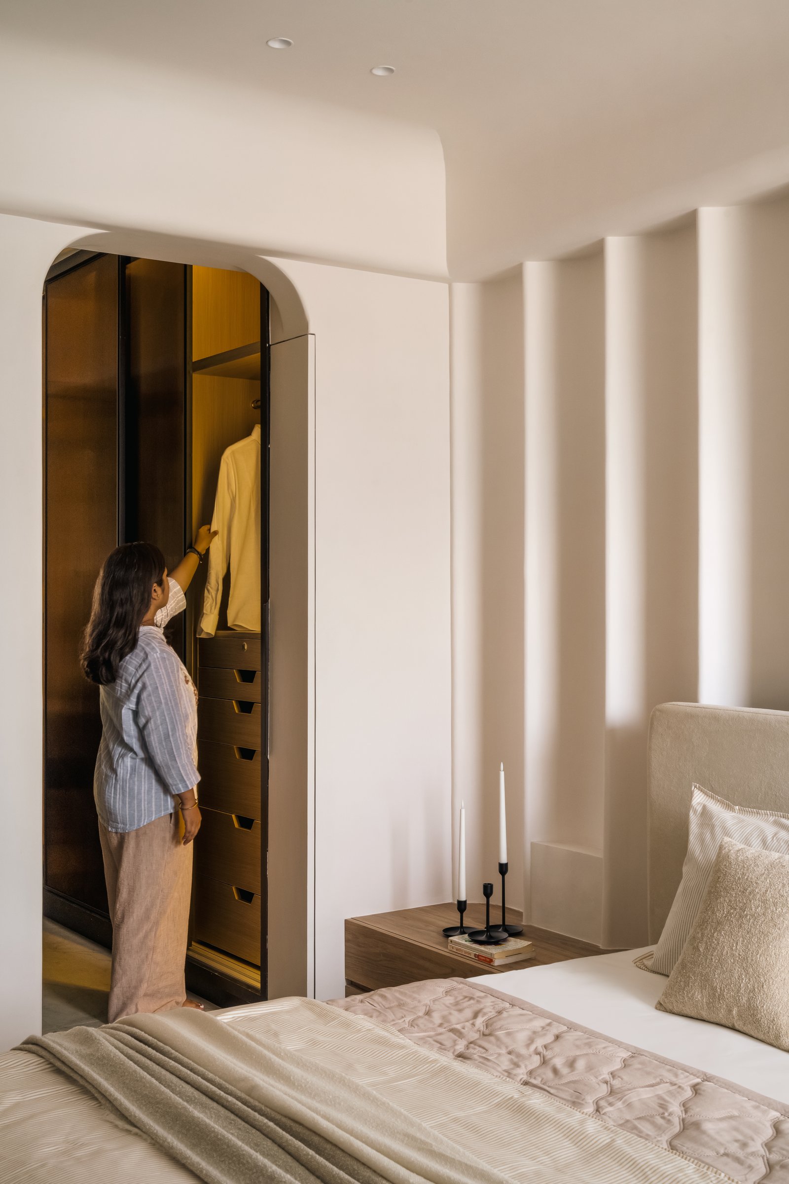 An arched wardrobe reveal, lined in bronze-toned finish, continues the room's vocabulary of eased geometry