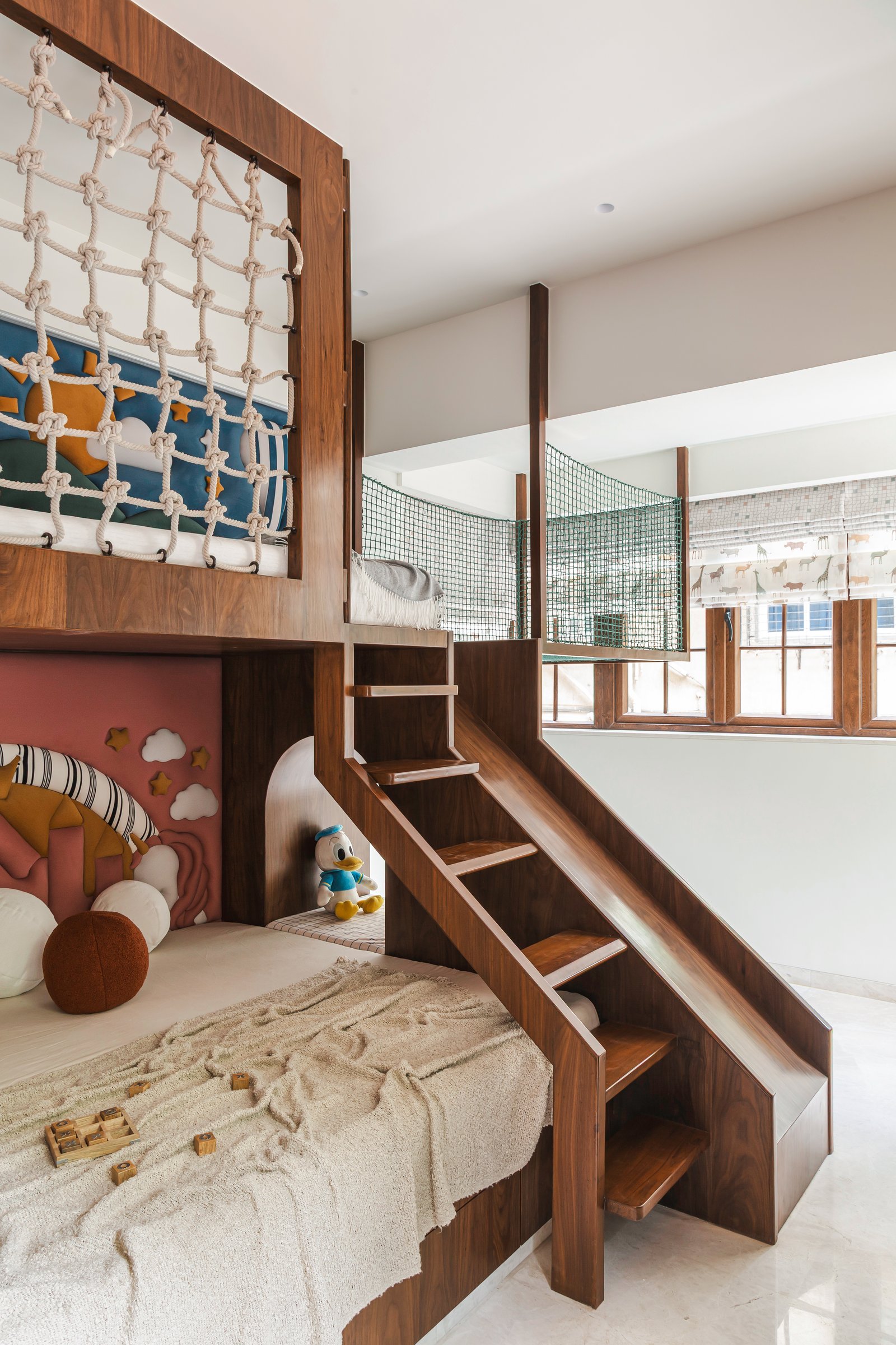 The children's room, where a wooden bunk-and-play structure stacks bed, rope net and curved slide into a single architectural piece