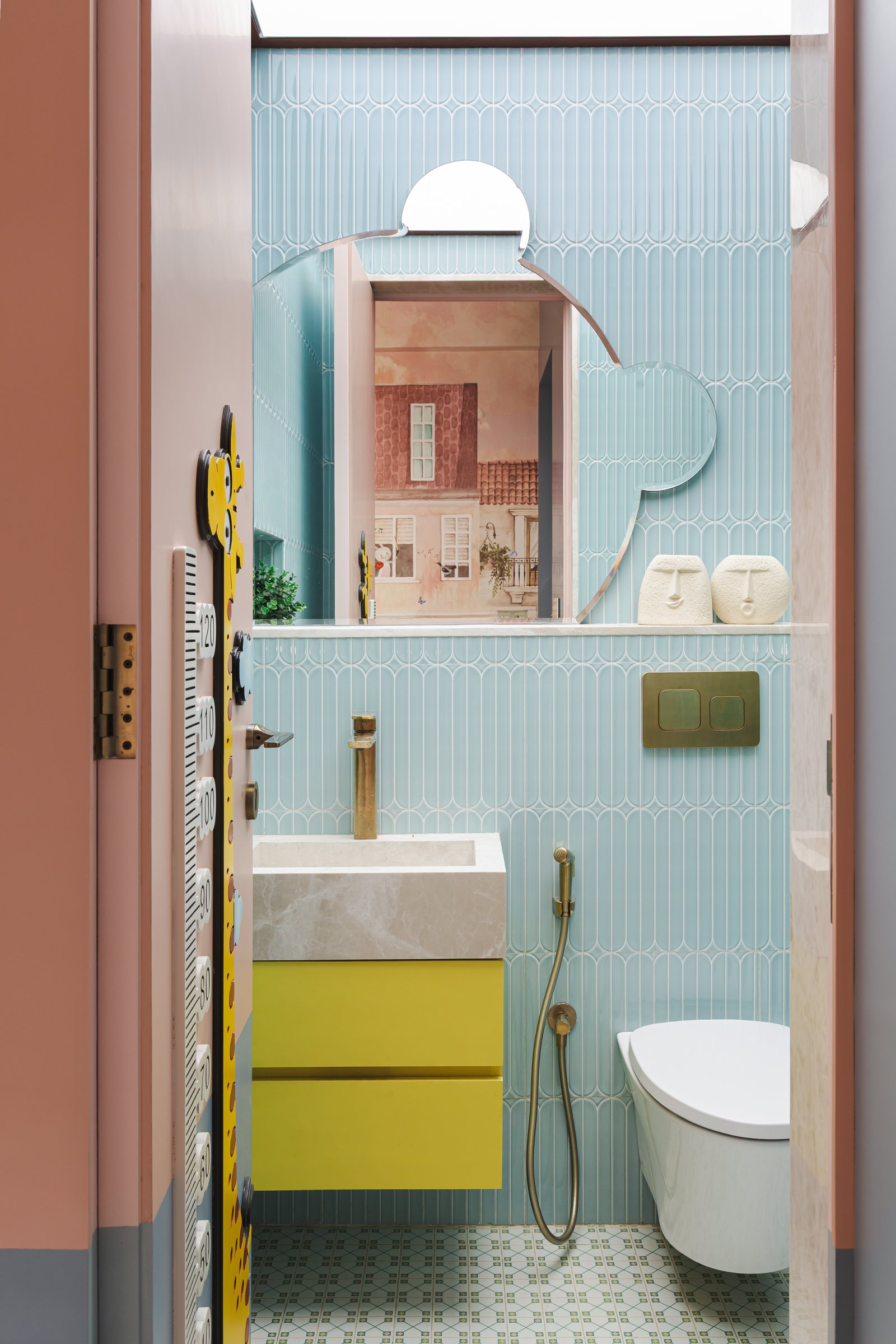 The children's bathroom, where fluted pale blue tile, a yellow vanity and a cloud-shaped mirror extend the playful register with discipline
