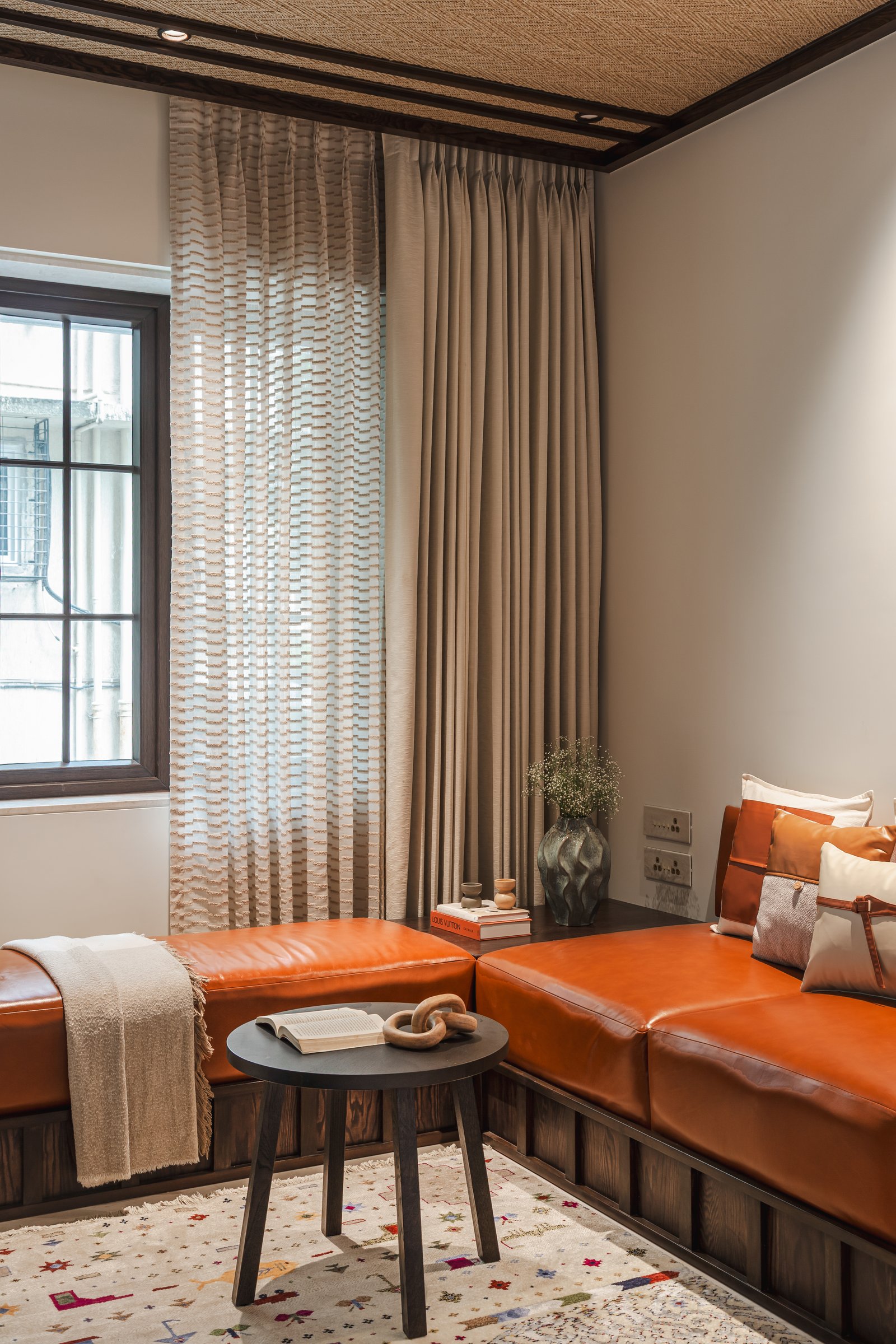 A built-in tan leather seating platform tucked beneath a tall window gives the compact living room a quieter, daybed-like corner