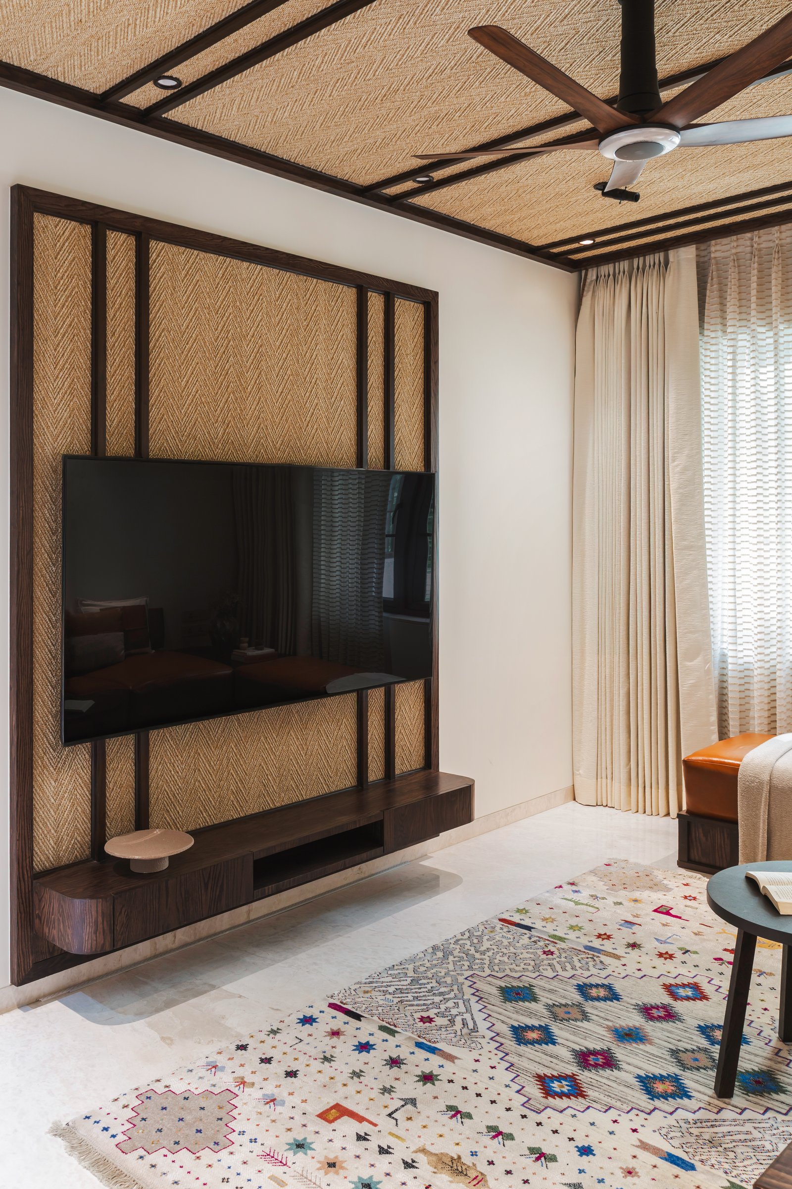 The living room, where a woven herringbone media wall and matching ceiling canopy bring warmth to the home's darker framework