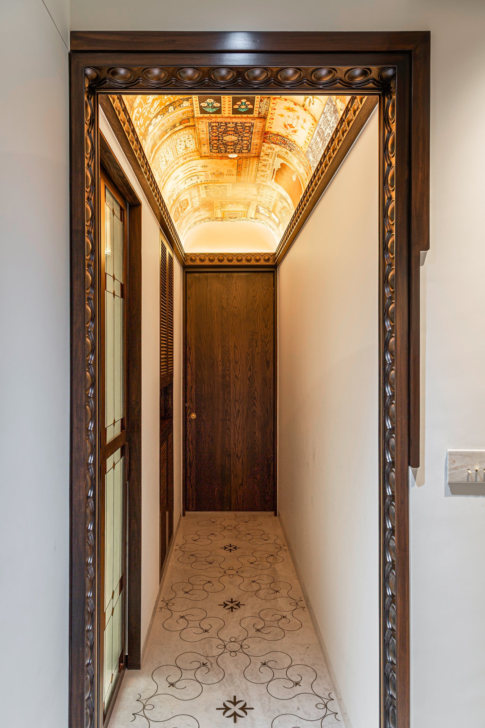 The entry, where a carved wooden frame, brass-inlaid marble floor and vaulted printed ceiling set the home's layered material language