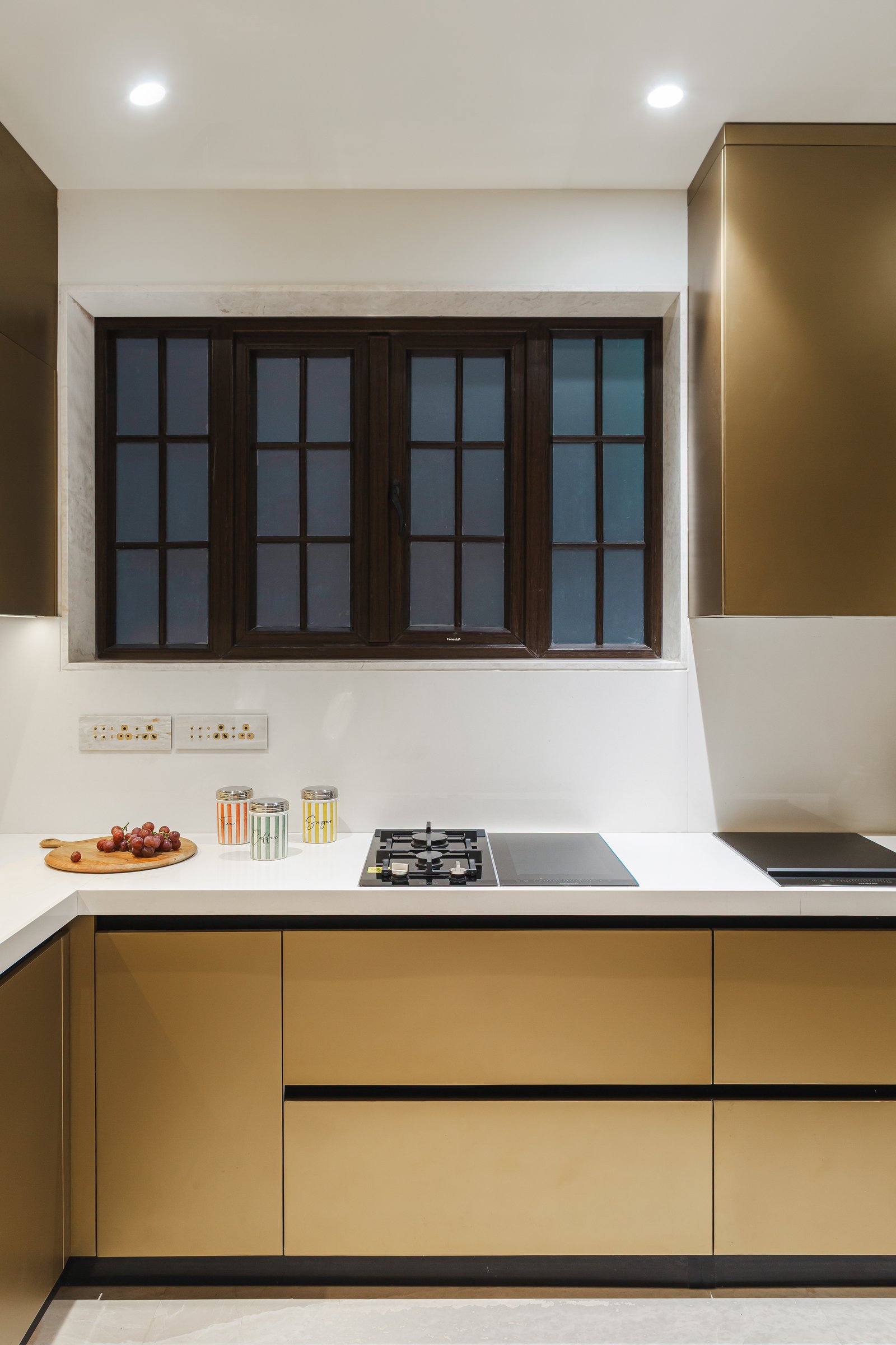 The kitchen, where handleless olive-gold cabinetry and white stone worktops take a restrained position within the home's wider material story