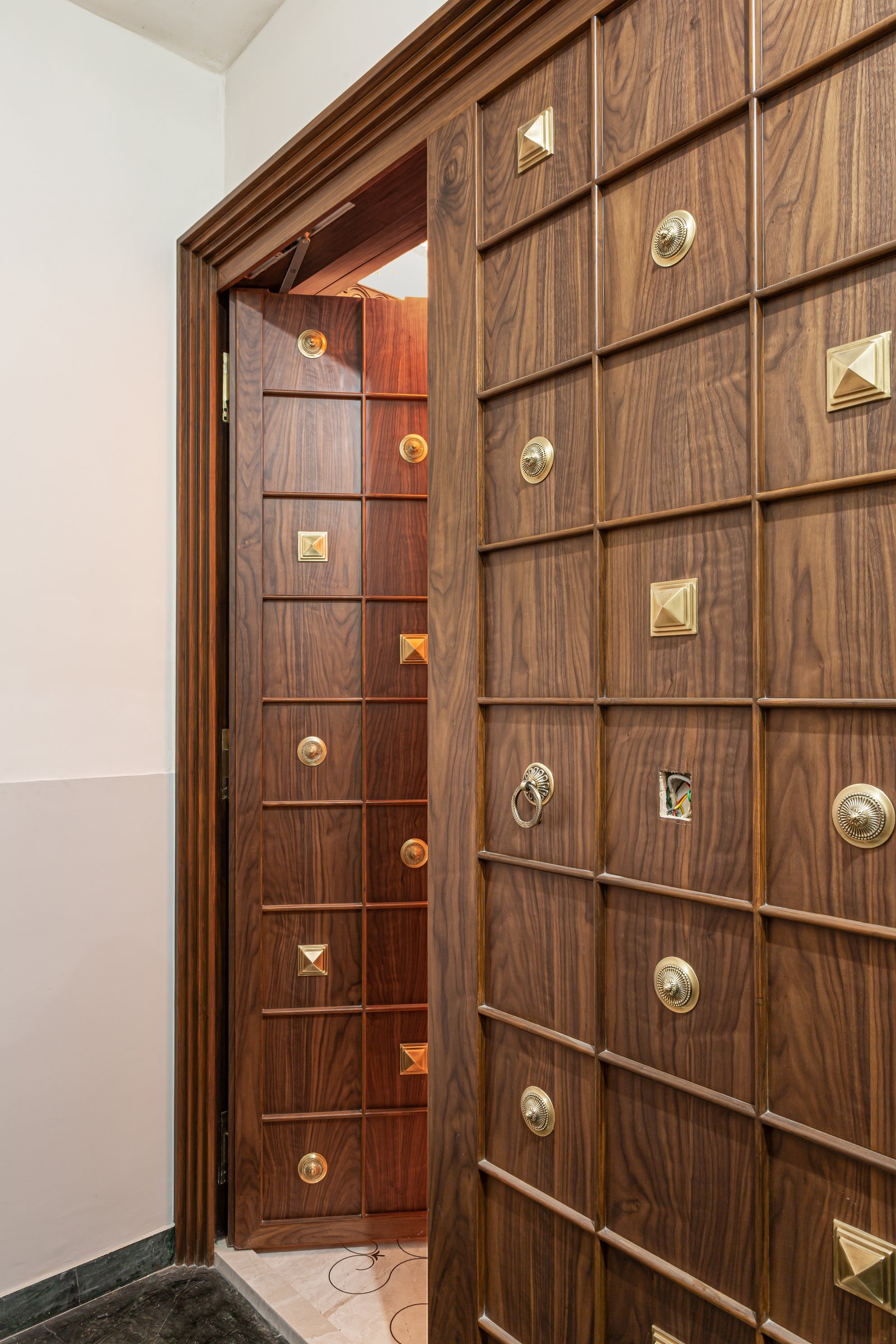The main door, a gridded wooden panel studded with brass medallions and bosses, where craft is treated as architecture rather than ornament