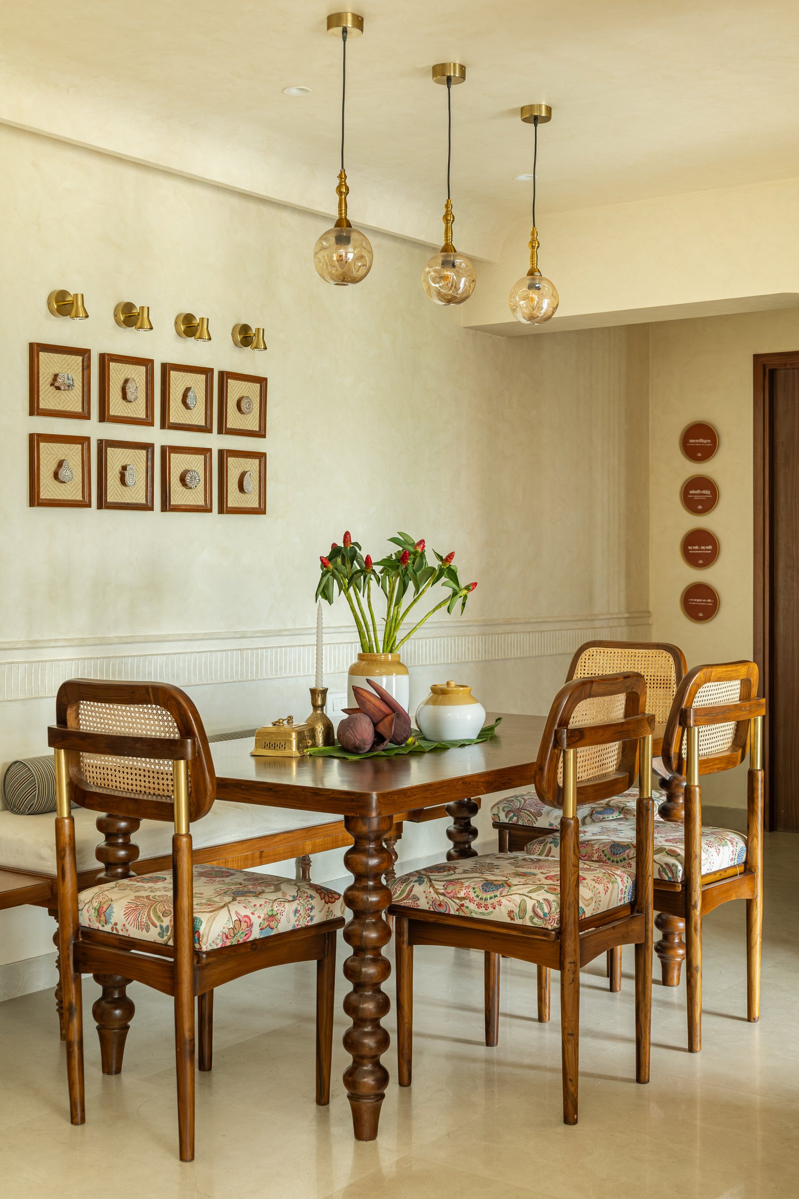 The dining area, where a turned-leg wooden table and cane-backed chairs sit beneath a line of amber globe pendants and a grid of framed craft objects