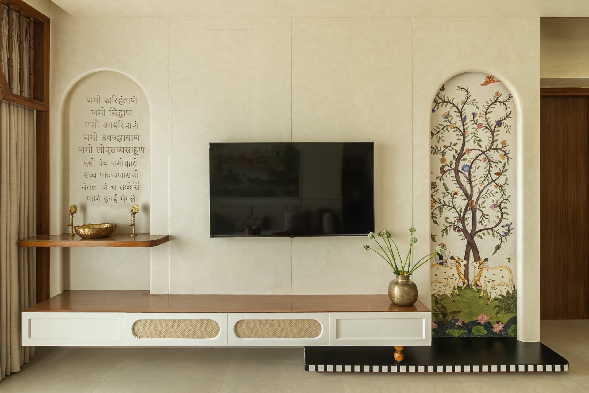The media wall, where a prayer inscription in low-relief lettering balances the Pichwai-inspired arched panel across the room