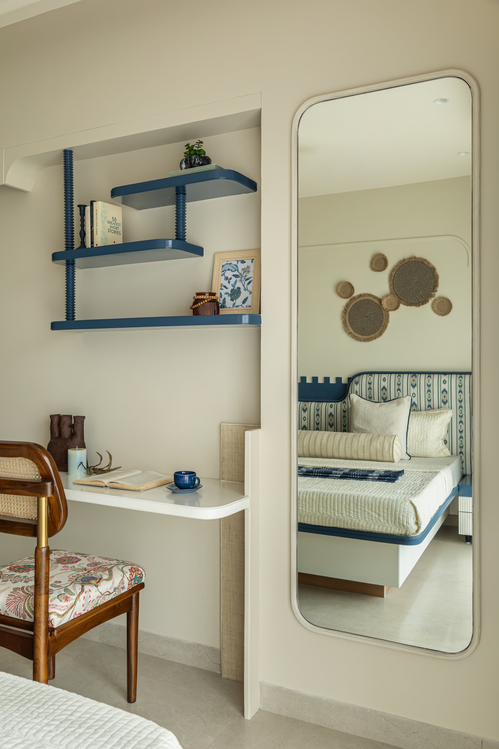 A compact study nook within the second bedroom, with a wall-mounted desk and cane-backed chair beneath indigo shelves