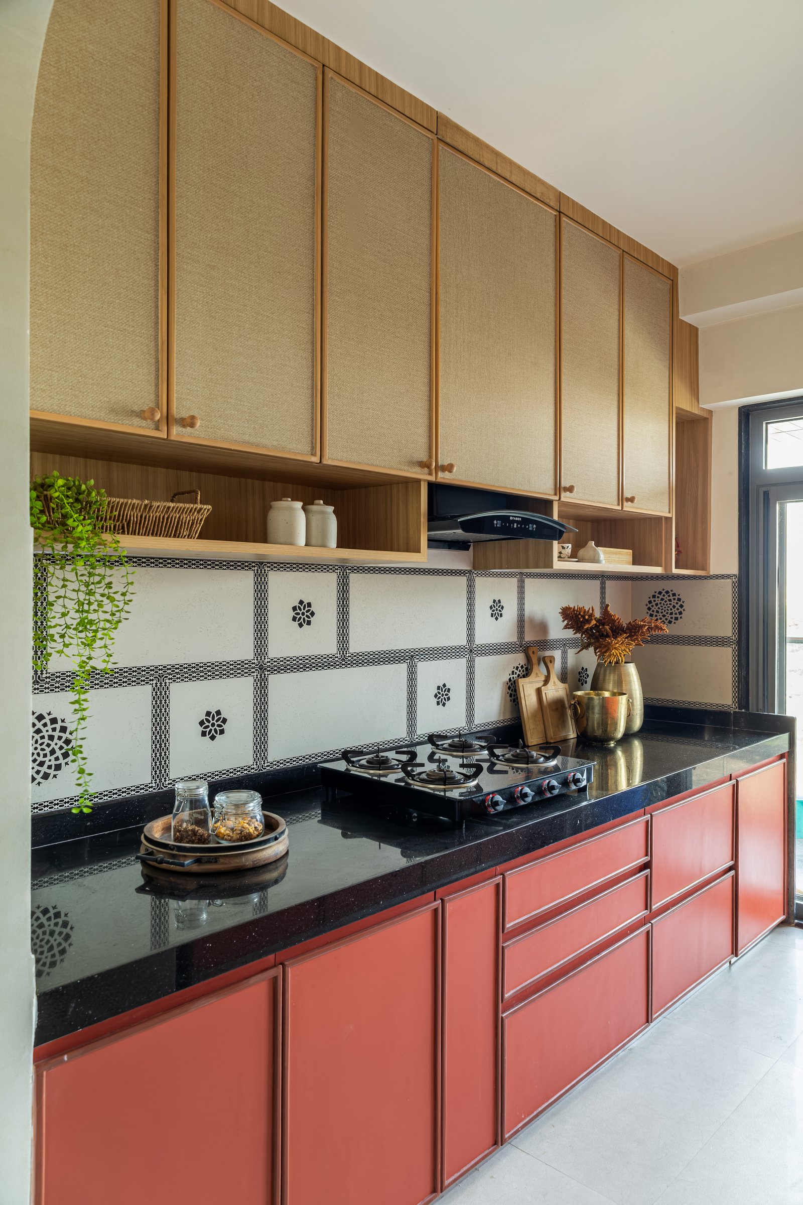 The kitchen, where terracotta-red cabinetry and woven-fronted overheads meet a patterned black-and-white backsplash