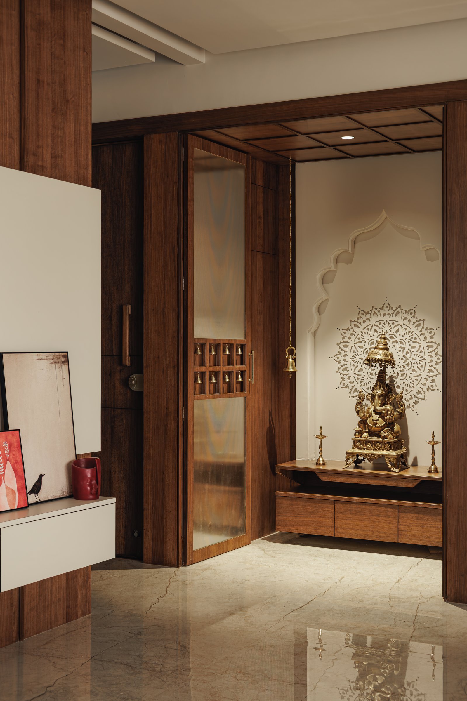 The puja space, framed by warm wooden panelling and a bifold door with brass bells