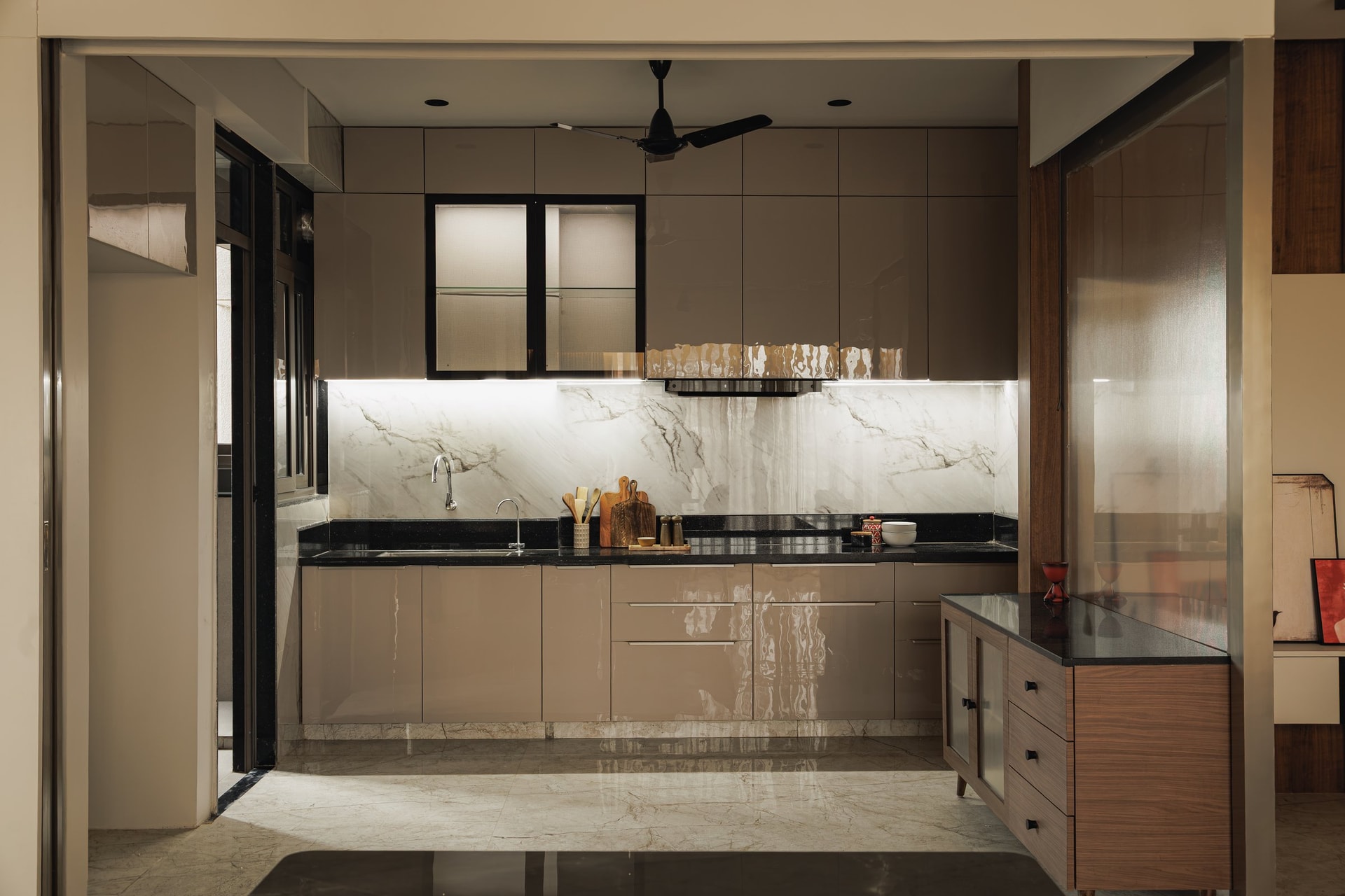 The kitchen, where high-gloss taupe cabinetry meets a book-matched marble backsplash and black stone counter