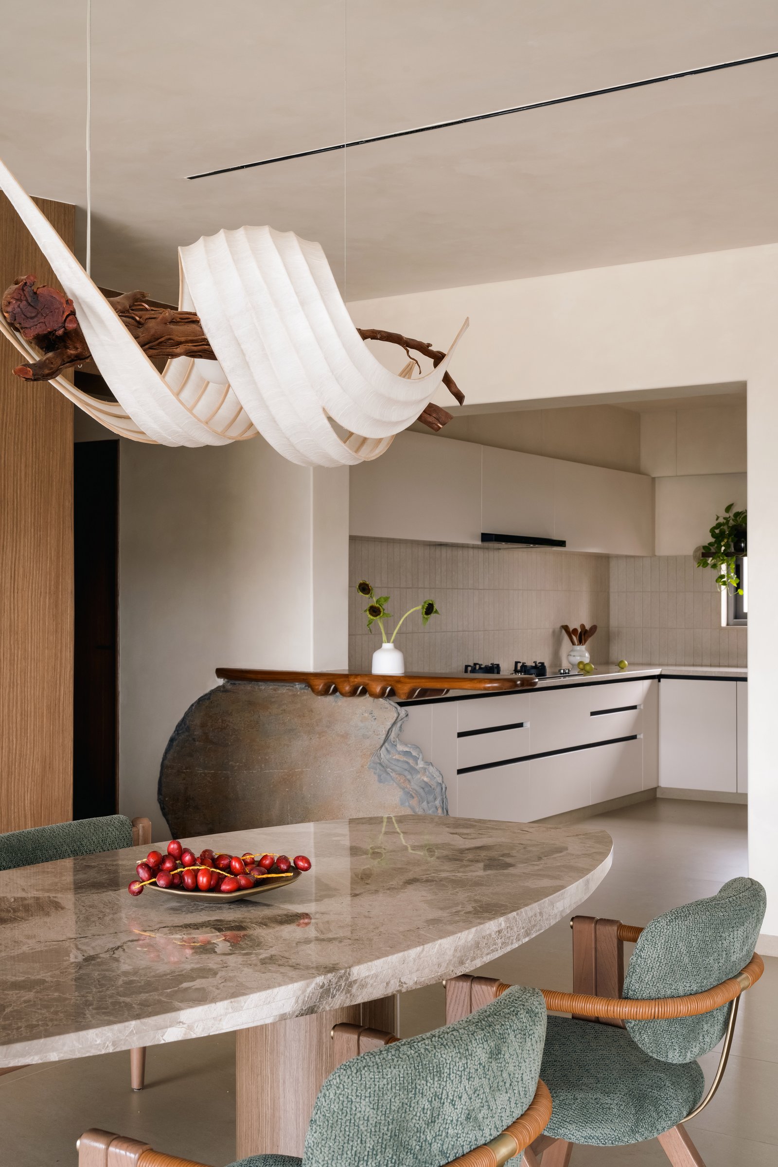 The dining area, pairing an irregular marble table with green upholstered chairs against the quieter kitchen beyond