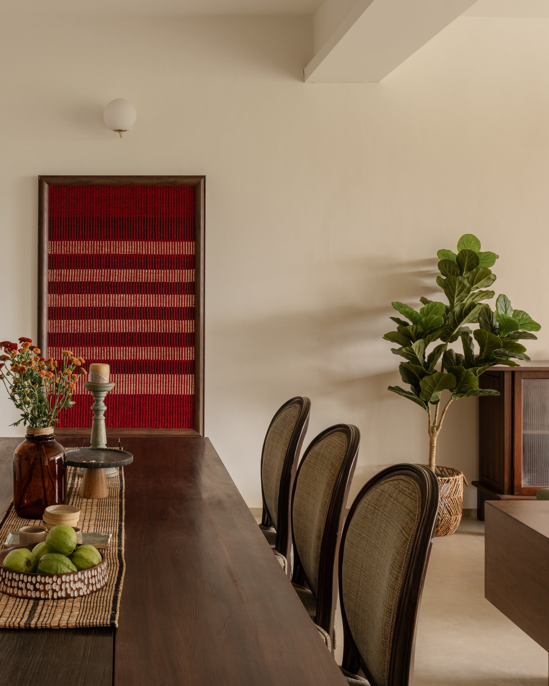The dining room's defining gesture: a tall framed textile in deep reds, hung at scale against the ivory wall