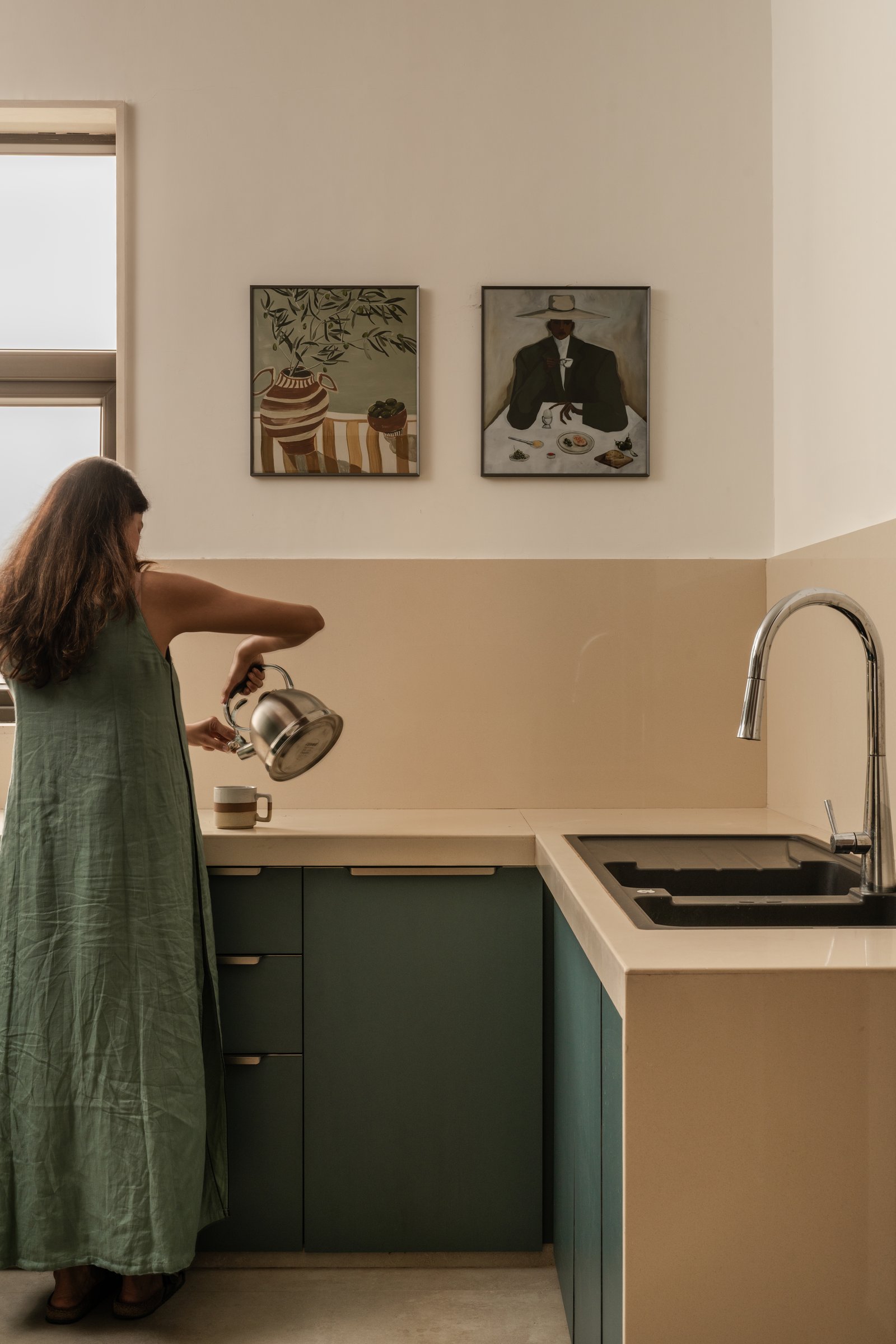The kitchen, where forest-green lower cabinetry meets a pale counter and a quiet pair of framed artworks above