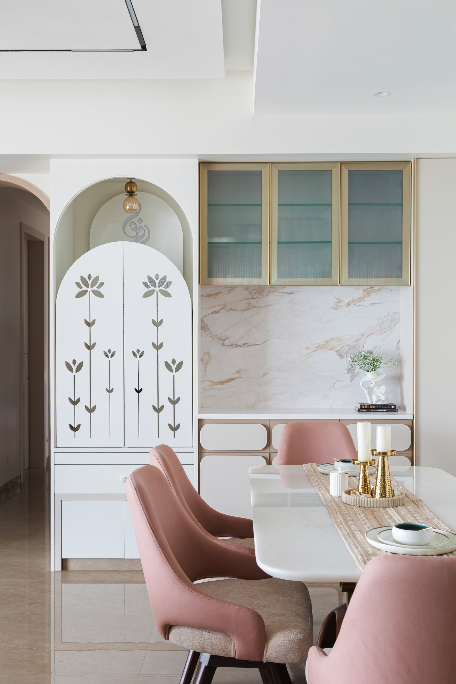 The dining area, flanked by the arched puja cabinet and a slim stone niche with brass-framed uppers